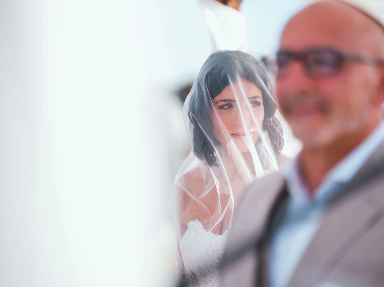 Le regard de la mariée sous son voile pendant la cérémonie religieuse, un invité flou au premier plan, mariage au Pavillon des Bains, Deauville, par Jean-Baptiste Argyre (Jaysphotography)