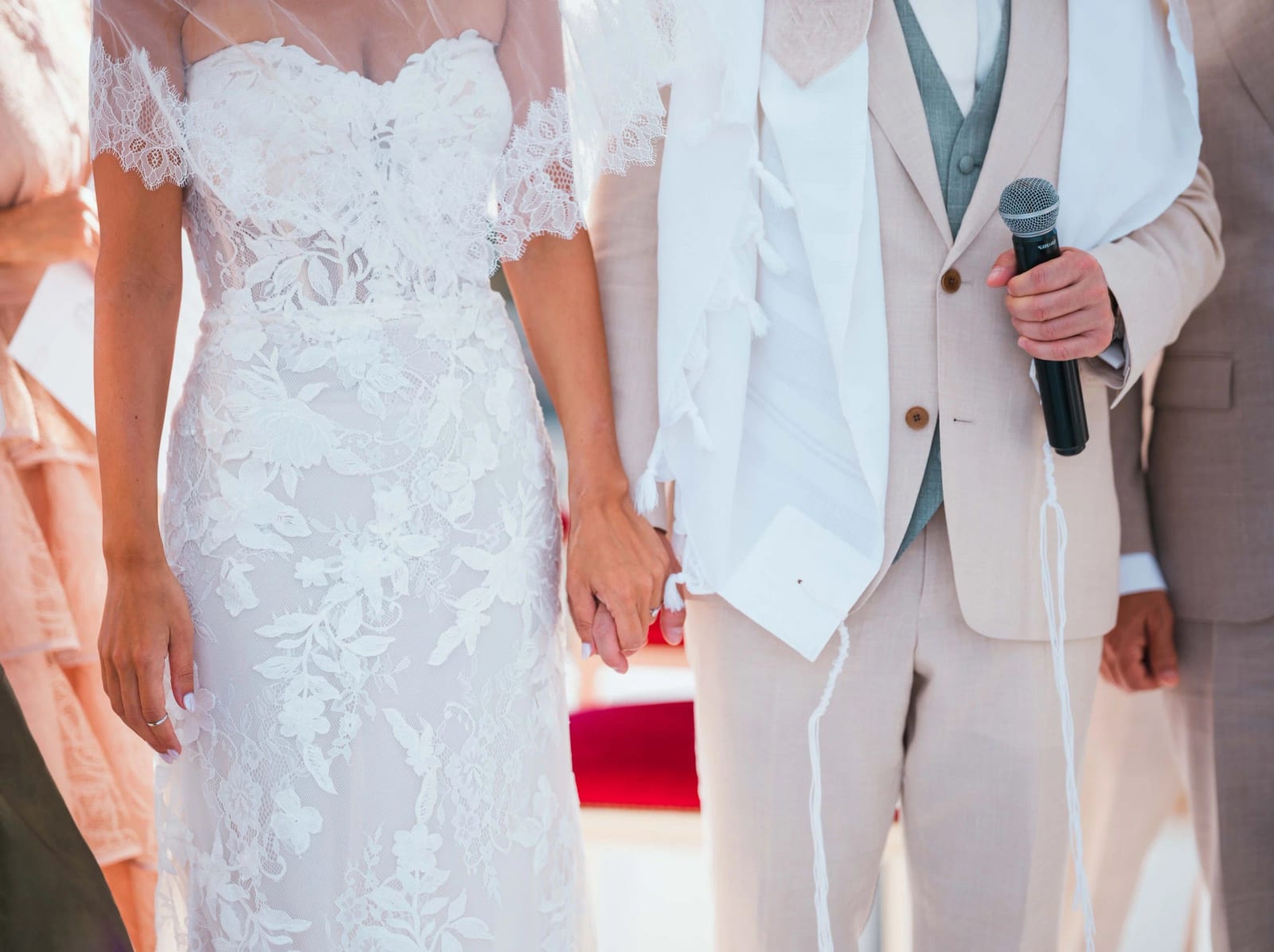Mains jointes des mariés, robe de dentelle et costume beige avec talith à franges, micro à la main, mariage au Pavillon des Bains, Deauville, par Jean-Baptiste Argyre (Jaysphotography)