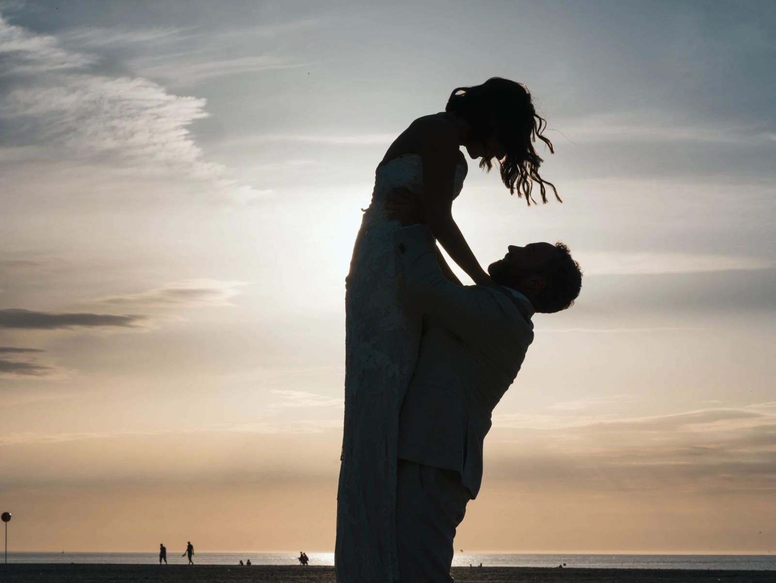 Silhouette du marié soulevant la mariée au coucher du soleil, promeneurs au bord de l'eau, mariage au Pavillon des Bains, Deauville, par Jean-Baptiste Argyre (Jaysphotography)