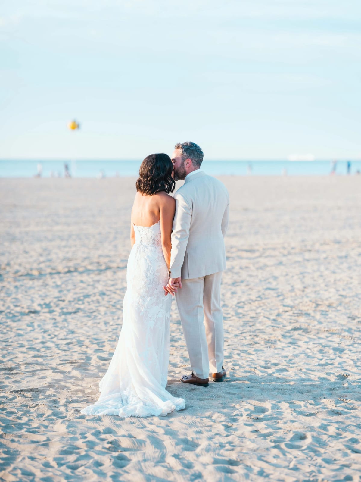 Les mariés de dos main dans la main face à la mer sur la plage de Deauville, mariage au Pavillon des Bains, Deauville, par Jean-Baptiste Argyre (Jaysphotography)