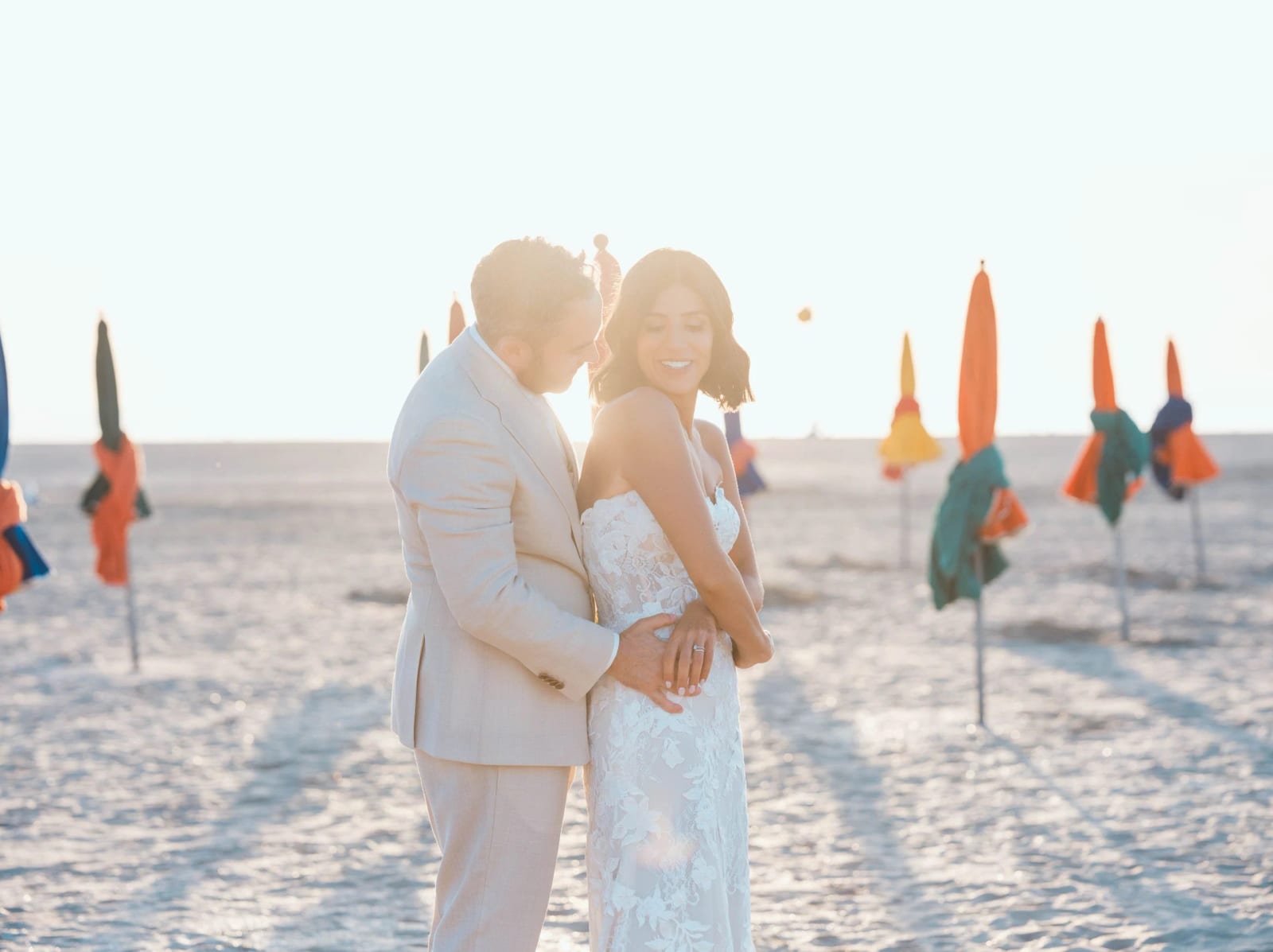 Les mariés enlacés au milieu des parasols refermés orange, vert et jaune de la plage de Deauville, mariage au Pavillon des Bains, Deauville, par Jean-Baptiste Argyre (Jaysphotography)