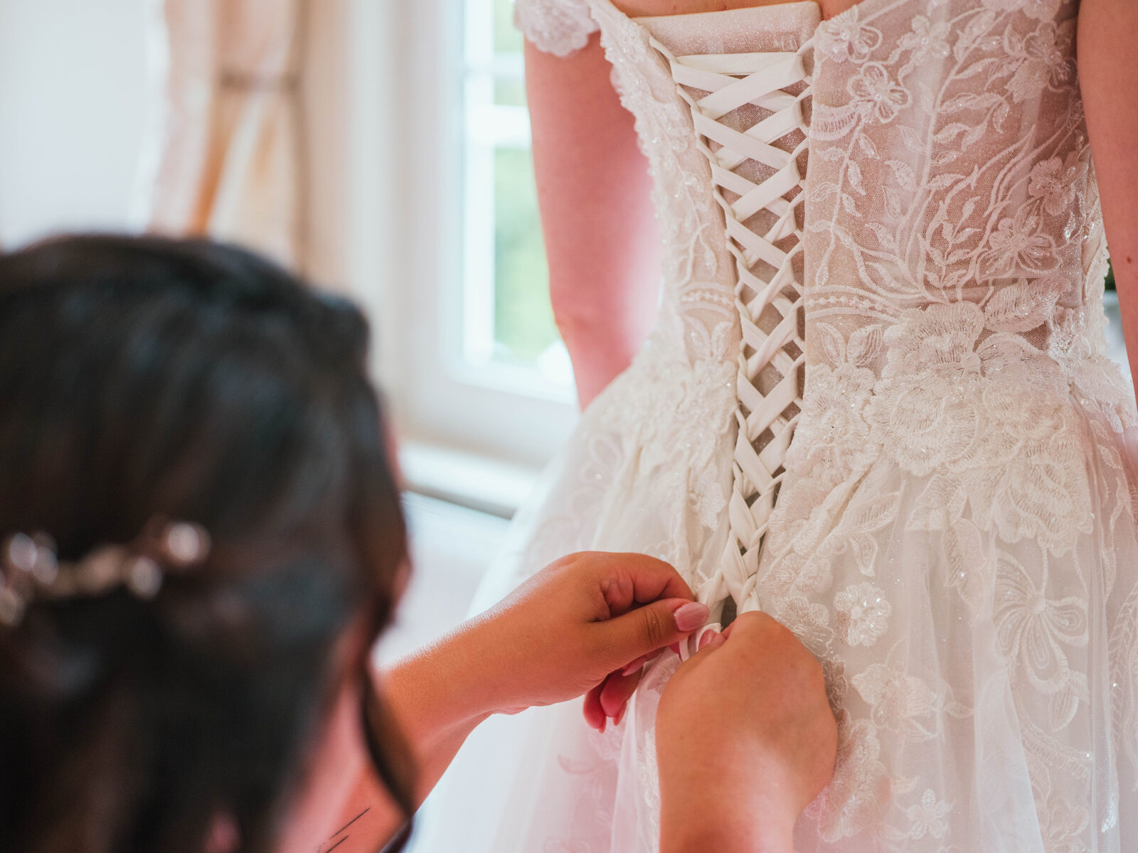 Laçage du corset en dentelle florale de la robe de mariée d'Émilie pendant l'habillage — mariage au Château de Naours, par Jean-Baptiste Argyre (Jaysphotography)