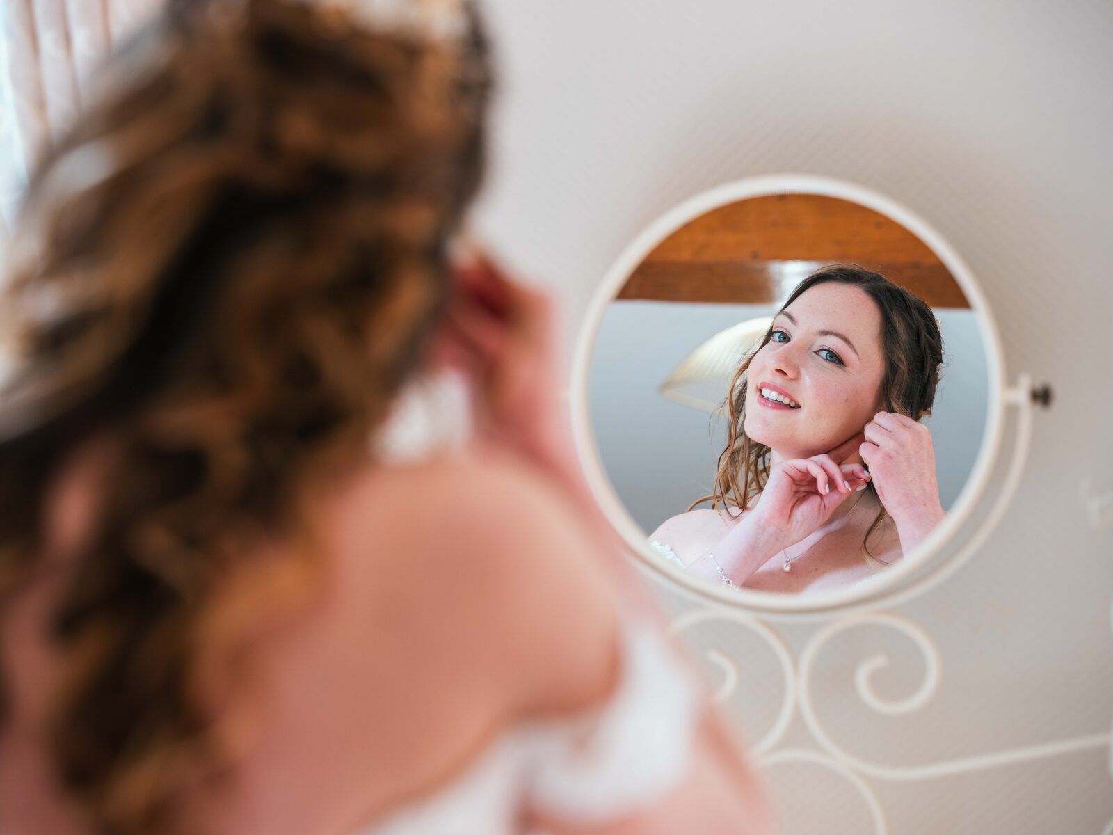 Émilie met ses boucles d'oreilles, son reflet capté dans un miroir rond lors des préparatifs — mariage au Château de Naours, par Jean-Baptiste Argyre (Jaysphotography)