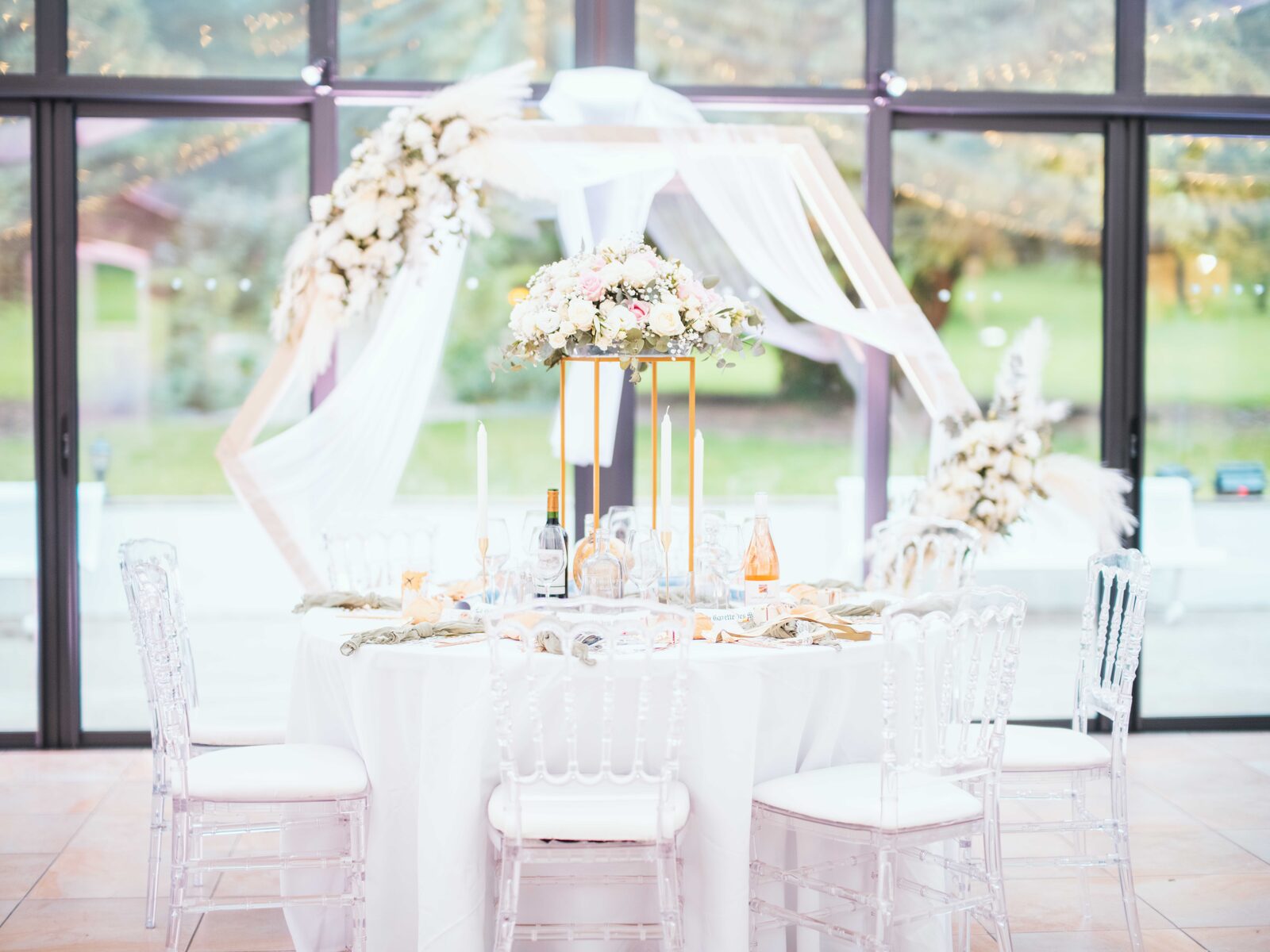 Table de réception dressée sous la verrière, centre floral et chaises Napoléon transparentes — mariage au Château de Naours, par Jean-Baptiste Argyre (Jaysphotography)