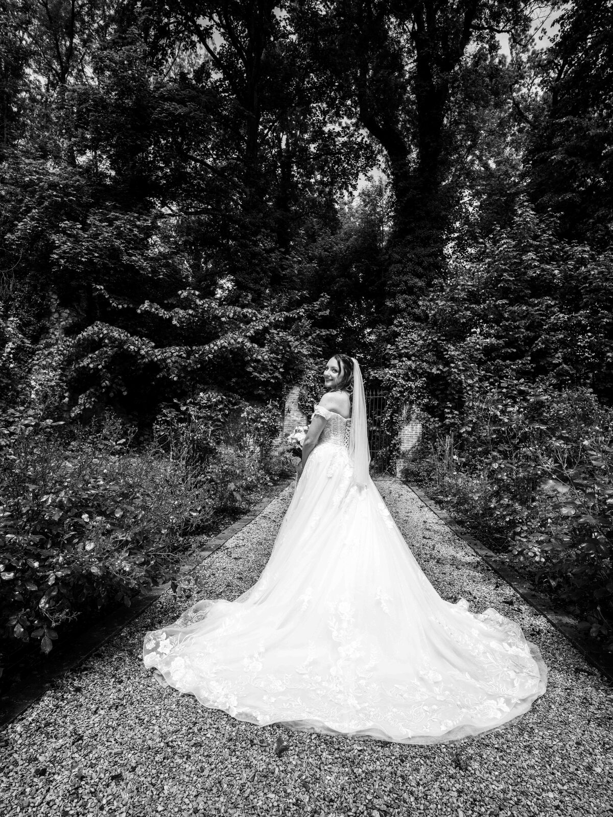 Portrait noir et blanc d'Émilie et sa longue traîne dans une allée arborée du parc — mariage au Château de Naours, par Jean-Baptiste Argyre (Jaysphotography)