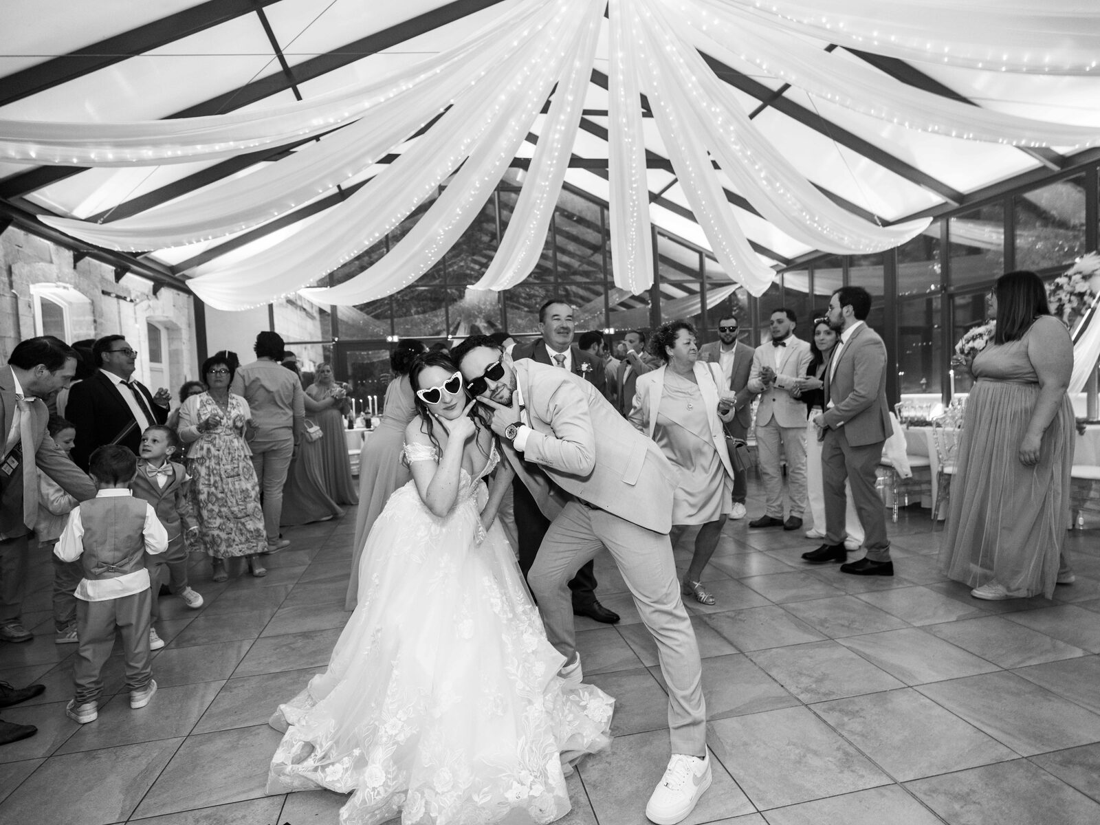 Grégory et Émilie sur la piste de danse, lunettes en cœur, entourés des invités, noir et blanc — mariage au Château de Naours, par Jean-Baptiste Argyre (Jaysphotography)