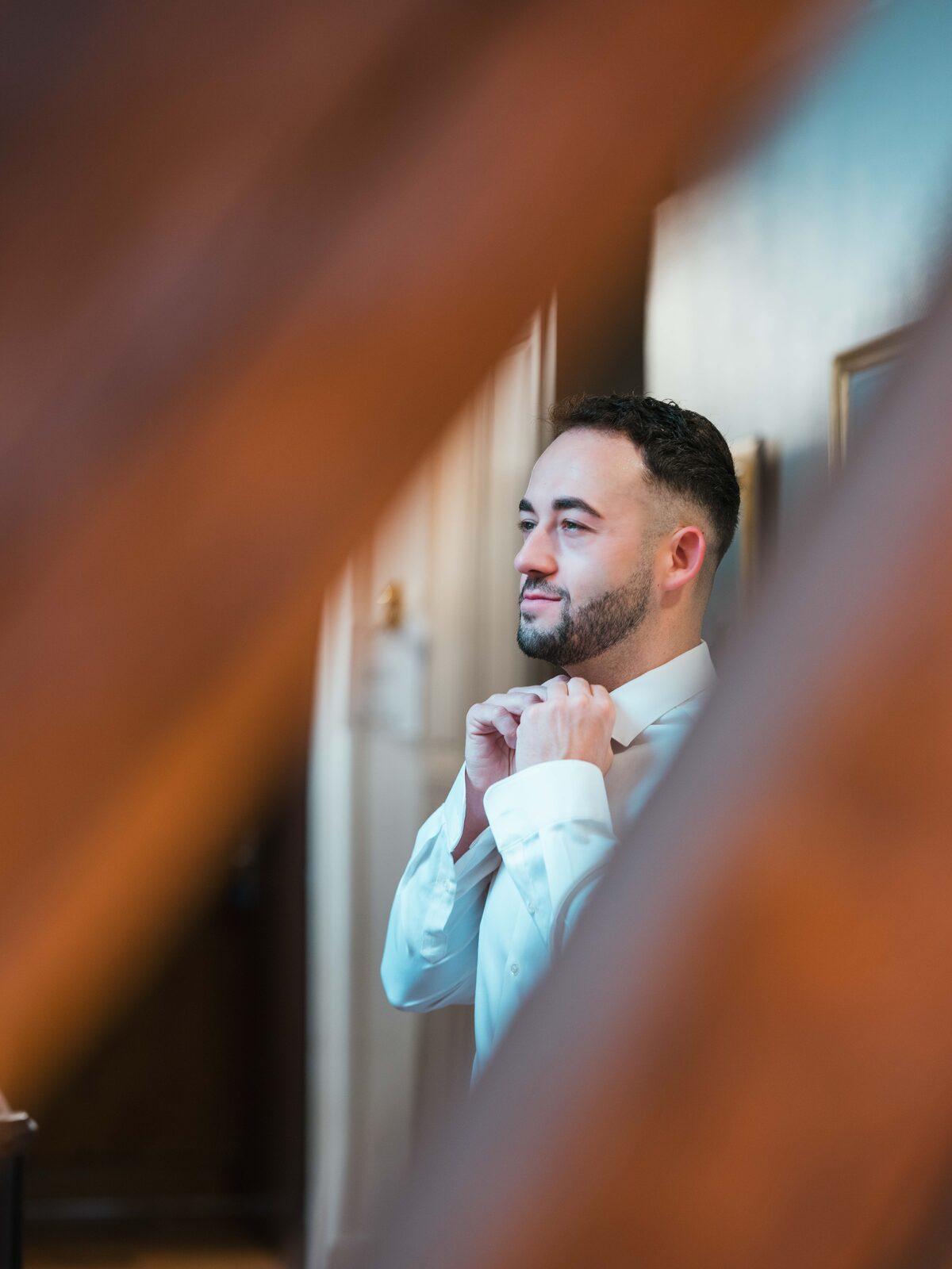 Portrait noir et blanc de Grégory ajustant son nœud papillon, vu à travers la rambarde — mariage au Château de Naours, par Jean-Baptiste Argyre (Jaysphotography)