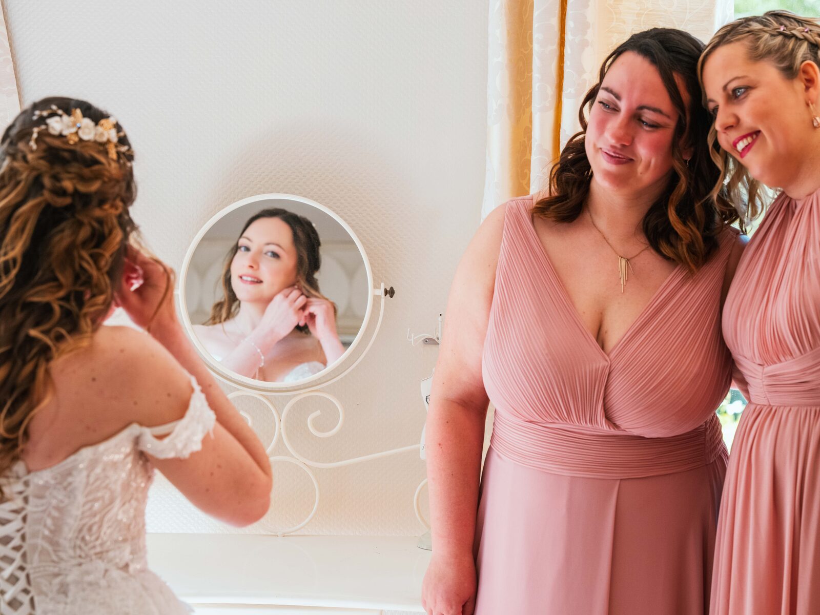 Émilie met ses boucles d'oreilles devant ses deux demoiselles d'honneur émues en robe rose — mariage au Château de Naours, par Jean-Baptiste Argyre (Jaysphotography)