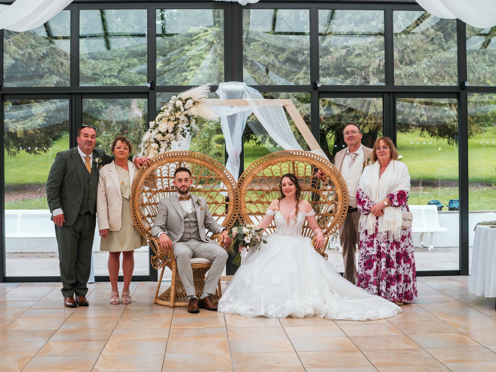 Photo de famille, les mariés sur fauteuils en rotin entourés de leurs parents sous la verrière — mariage au Château de Naours, par Jean-Baptiste Argyre (Jaysphotography)