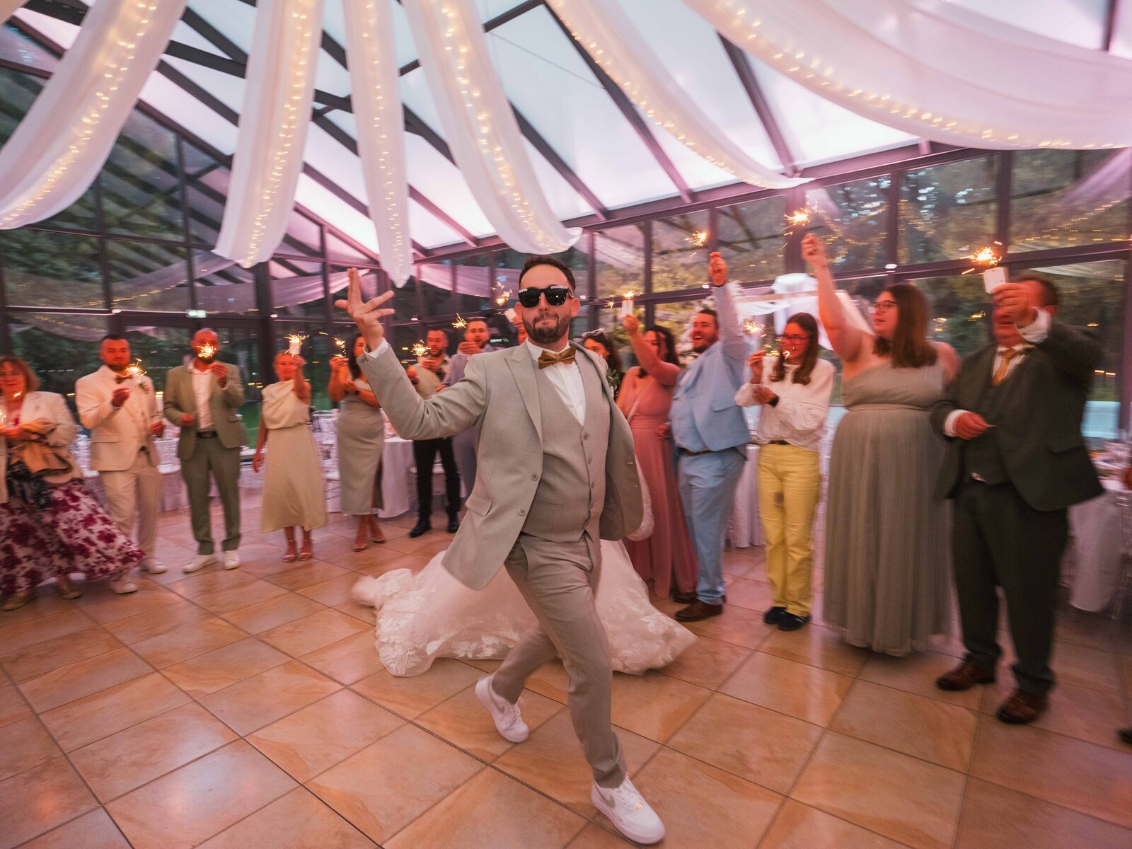 Entrée dansante de Grégory en lunettes de soleil, invités levant leurs cierges magiques — mariage au Château de Naours, par Jean-Baptiste Argyre (Jaysphotography)