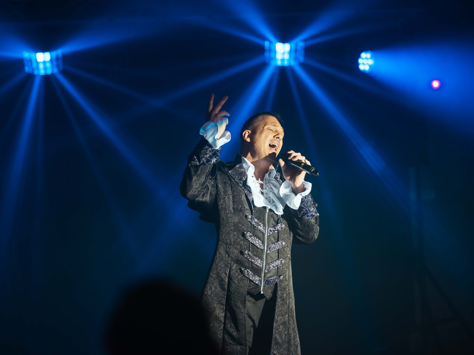 Le transformiste Thony Lymer chante sur scène en costume baroque sous les lumières bleues — mariage au Château de Naours, par Jean-Baptiste Argyre (Jaysphotography)