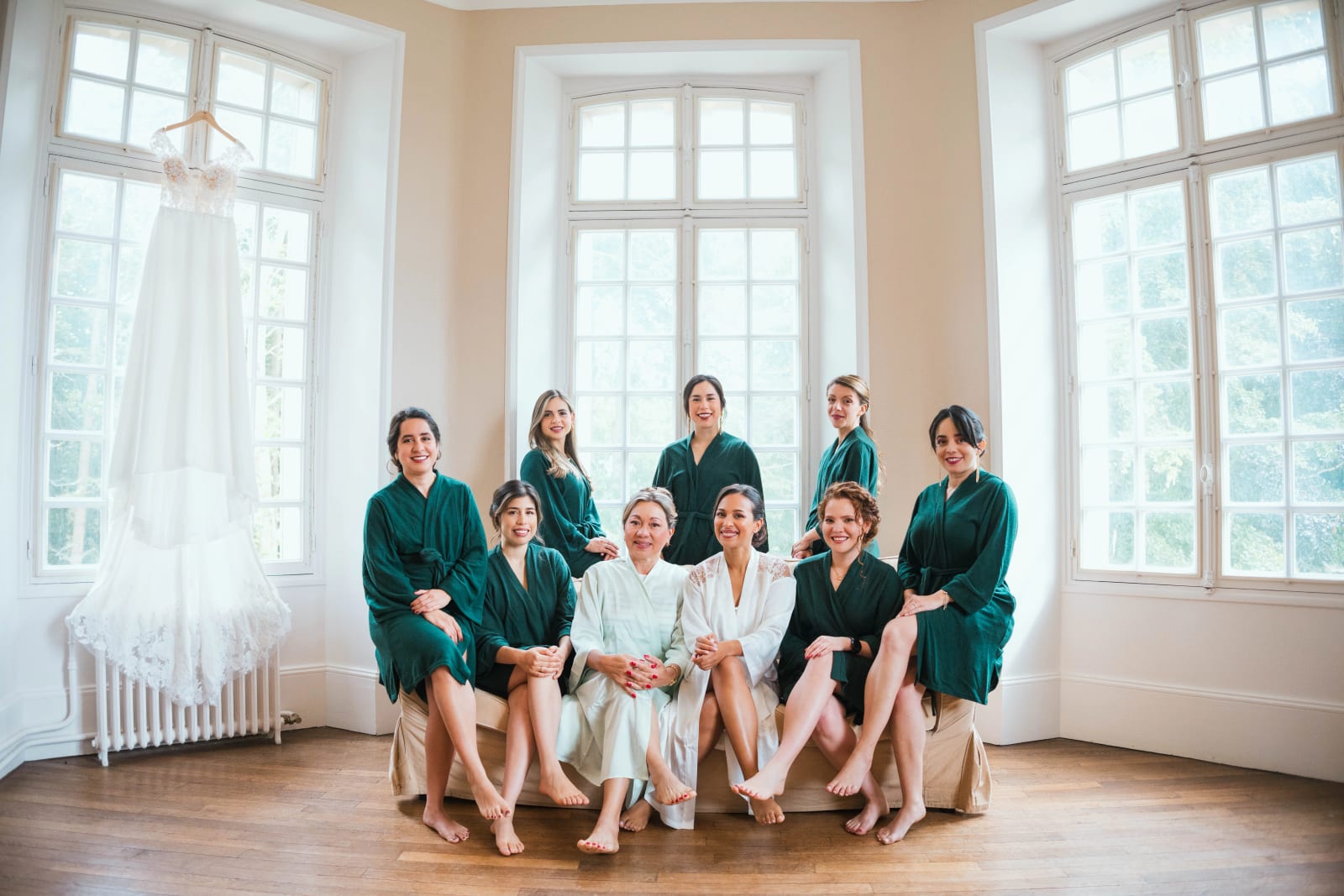 Les demoiselles d'honneur en peignoirs vert émeraude posent autour d'Ana et d'une proche en peignoir clair, la robe de mariée suspendue à gauche, dans un grand salon du château, mariage au Domaine d'Orgival, par Jean-Baptiste Argyre (Jaysphotography)
