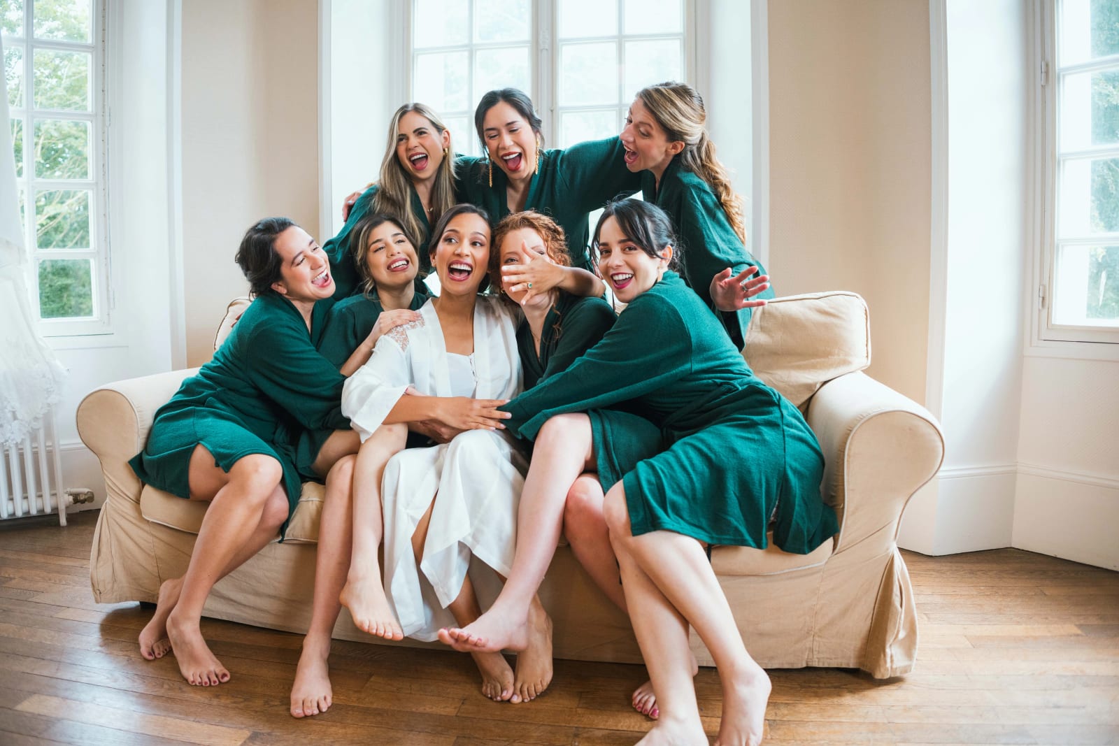 Ana en peignoir clair au centre du canapé, entourée de ses demoiselles d'honneur en peignoirs vert émeraude, toutes en plein fou rire, mariage au Domaine d'Orgival, par Jean-Baptiste Argyre (Jaysphotography)