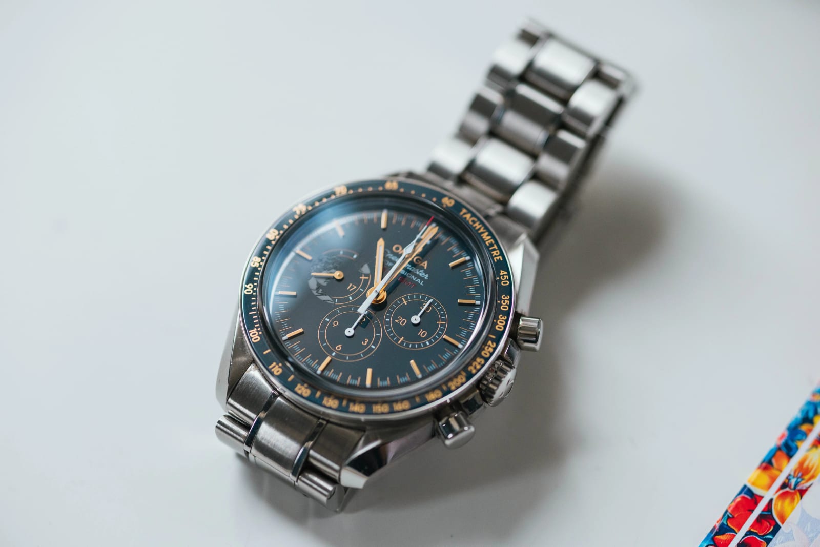 Détail de la montre chronographe Omega au cadran bleu du marié, posée près d'une pochette colorée, mariage au Domaine d'Orgival, par Jean-Baptiste Argyre (Jaysphotography)