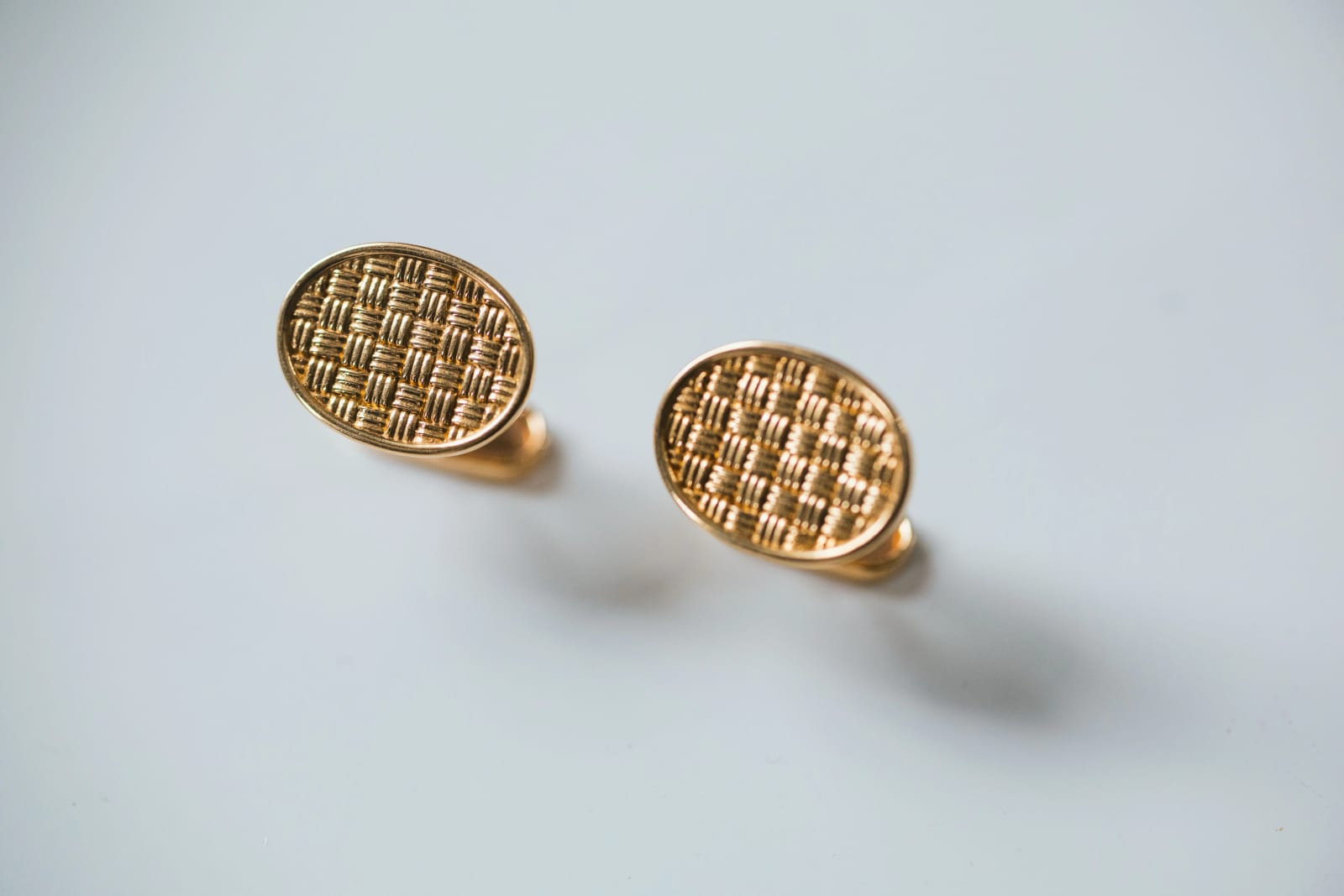 Gros plan sur les boutons de manchette ovales tressés d'or de Guillaume, posés sur une table blanche, mariage au Domaine d'Orgival, par Jean-Baptiste Argyre (Jaysphotography)