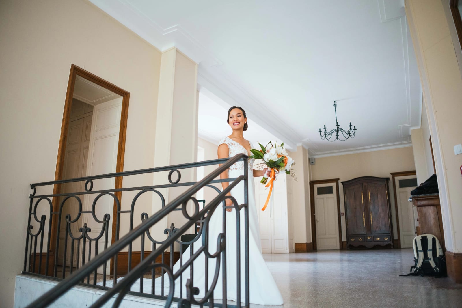 Ana descend le grand escalier en fer forgé du château, robe et bouquet à la main, rayonnante, mariage au Domaine d'Orgival, par Jean-Baptiste Argyre (Jaysphotography)