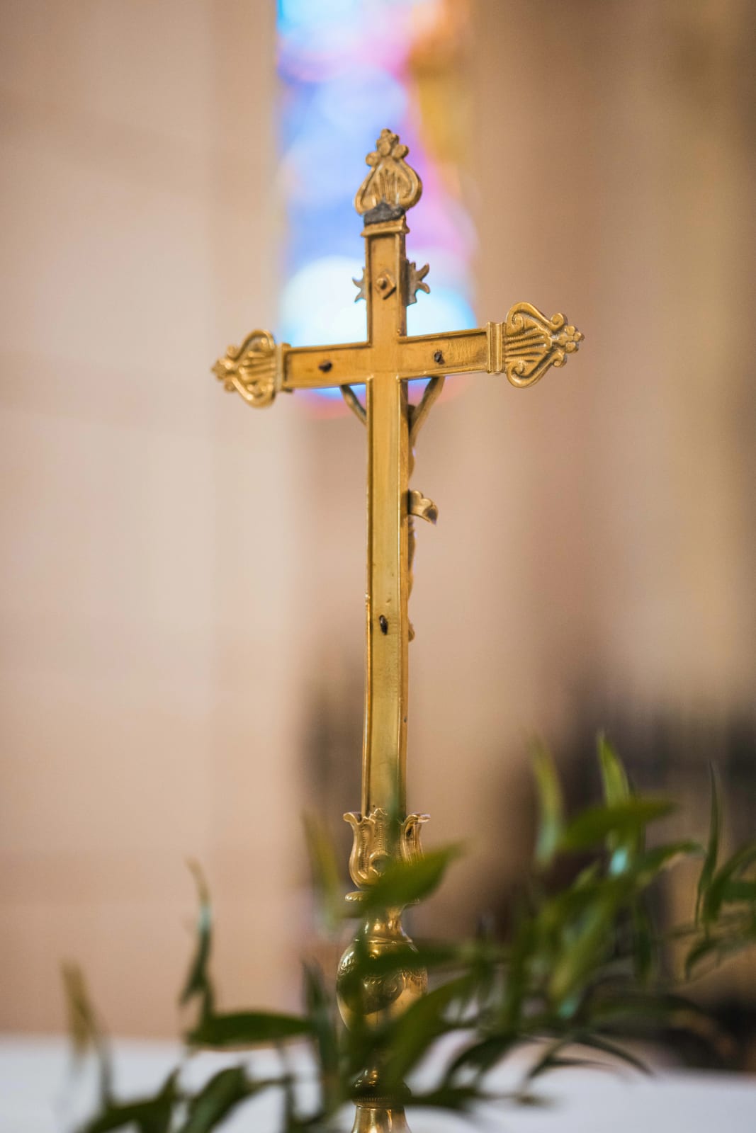 Croix dorée de l'autel de l'église d'Ambleny, vitrail coloré en arrière-plan, feuillage vert au premier plan, mariage au Domaine d'Orgival, par Jean-Baptiste Argyre (Jaysphotography)