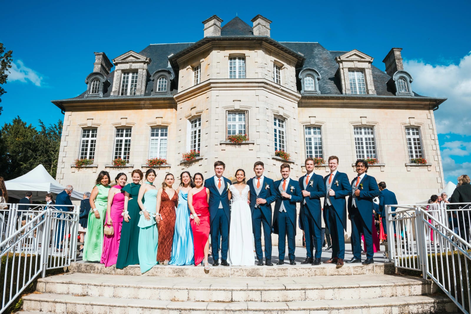 Photo de groupe de tout le cortège, demoiselles d'honneur en robes colorées et garçons d'honneur en costume bleu, sur le perron du château, mariage au Domaine d'Orgival, par Jean-Baptiste Argyre (Jaysphotography)