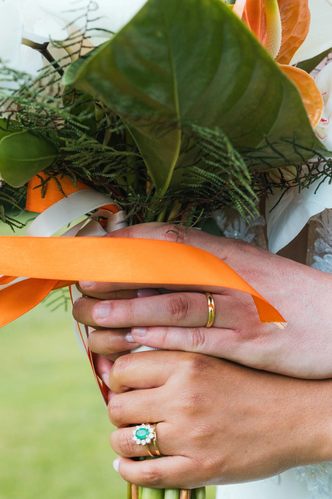 Détail des mains des mariés tenant le bouquet noué d'un ruban orange, bague de fiançailles à l'émeraude au doigt d'Ana, mariage au Domaine d'Orgival, par Jean-Baptiste Argyre (Jaysphotography)