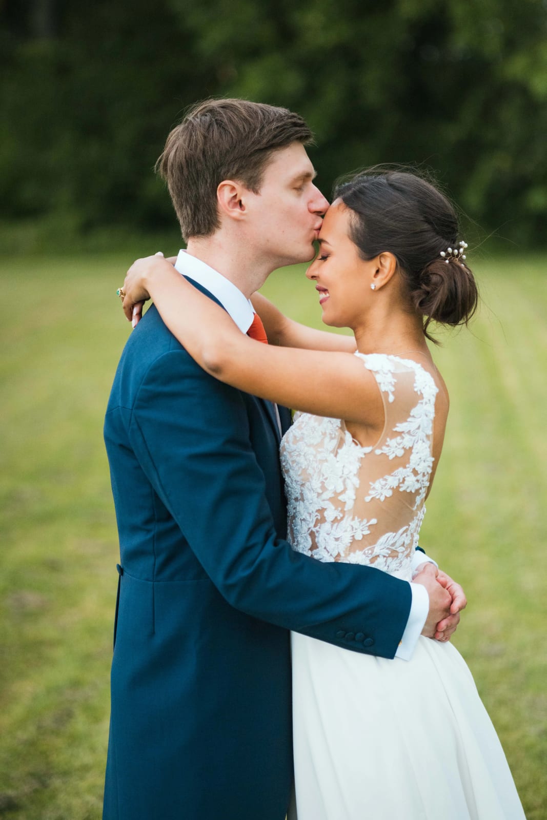 Guillaume embrasse le front d'Ana qui l'enlace, le dos en dentelle de la robe bien visible, dans la verdure du parc, mariage au Domaine d'Orgival, par Jean-Baptiste Argyre (Jaysphotography)
