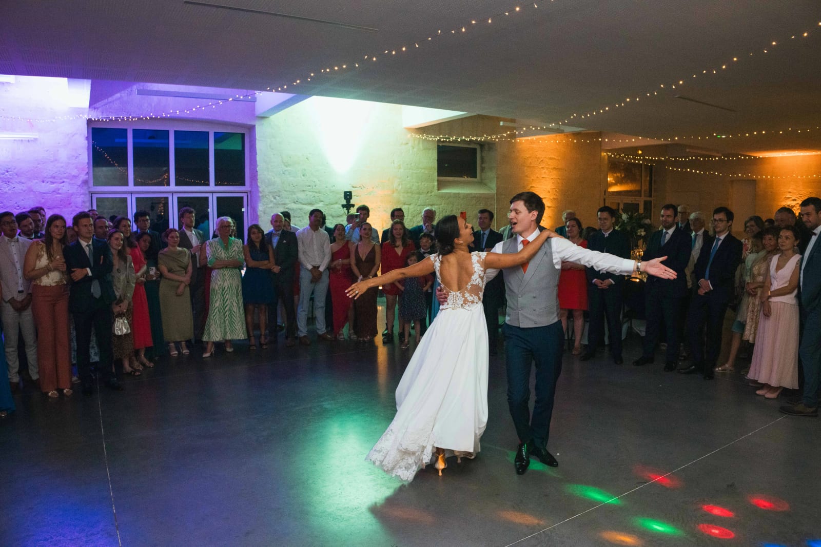 Ouverture de bal vue large : Ana et Guillaume dansent bras ouverts au centre de la piste, entourés des invités sous les jeux de lumière, mariage au Domaine d'Orgival, par Jean-Baptiste Argyre (Jaysphotography)