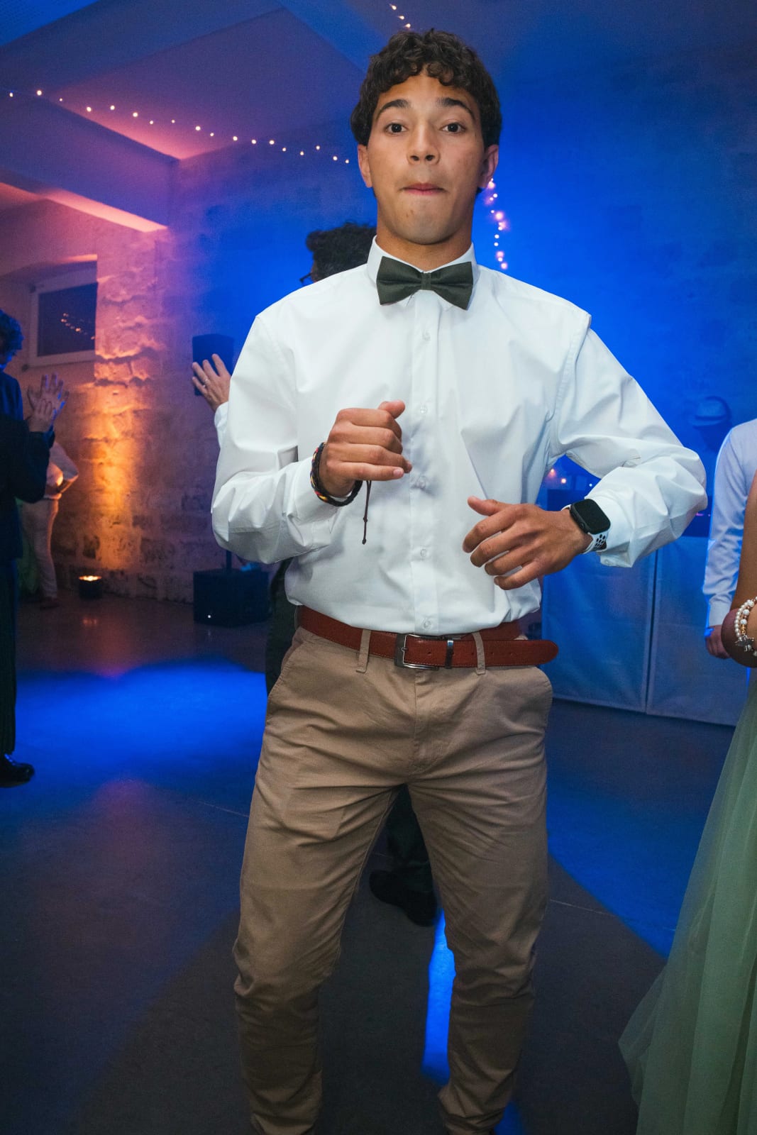 Un jeune invité en chemise blanche et nœud papillon danse avec énergie face à l'objectif sous les lumières bleues, mariage au Domaine d'Orgival, par Jean-Baptiste Argyre (Jaysphotography)