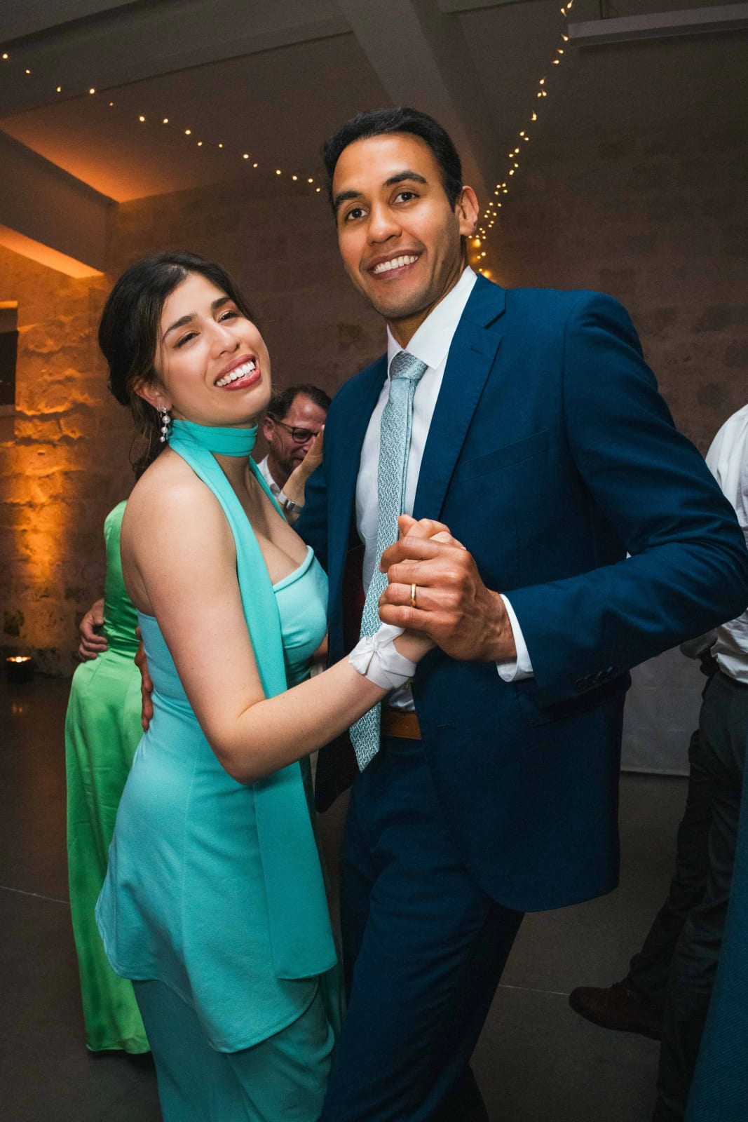 Une invitée en robe turquoise et un invité en costume bleu dansent en souriant à l'objectif pendant la soirée, mariage au Domaine d'Orgival, par Jean-Baptiste Argyre (Jaysphotography)