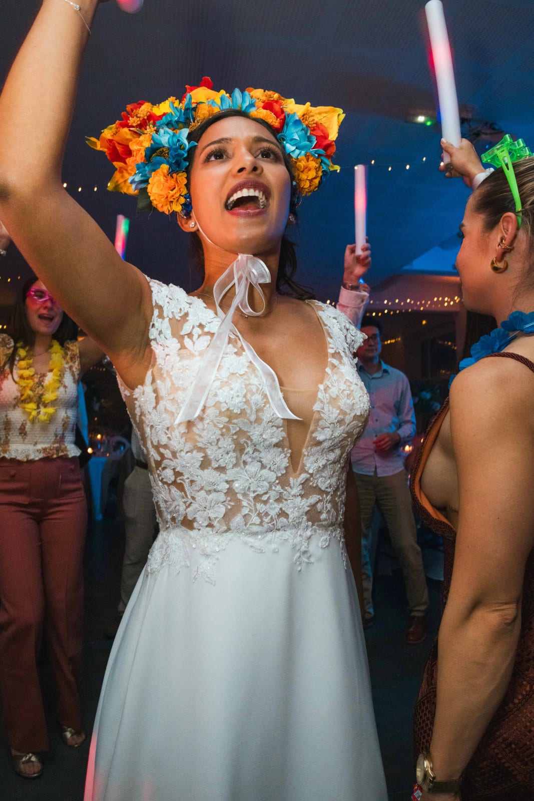 Ana, couronne de fleurs colorées sur la tête, chante bras levé au cœur de La Hora Loca, entourée d'invités munis de bâtons lumineux, mariage au Domaine d'Orgival, par Jean-Baptiste Argyre (Jaysphotography)