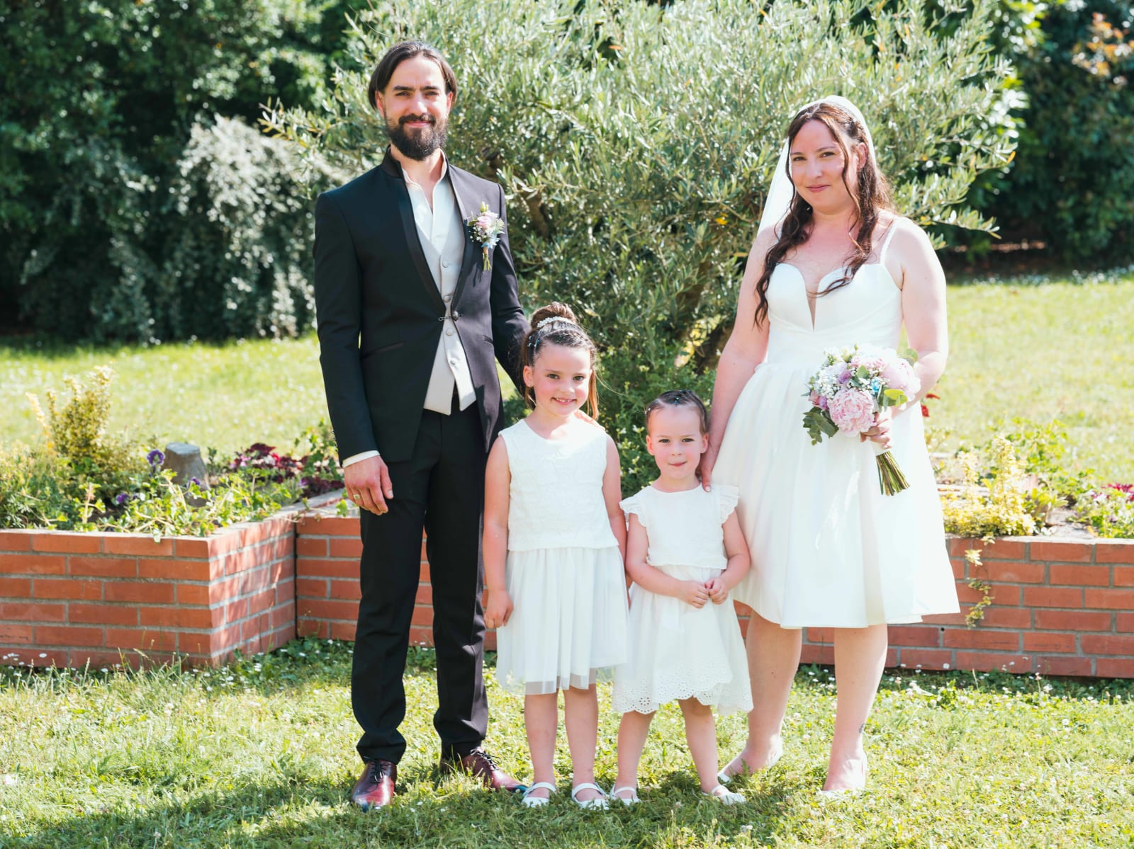 Les mariés posant avec les enfants d'honneur en blanc dans le jardin, mariage au Domaine de l'Orangerie de Villette, par Jean-Baptiste Argyre (Jaysphotography)