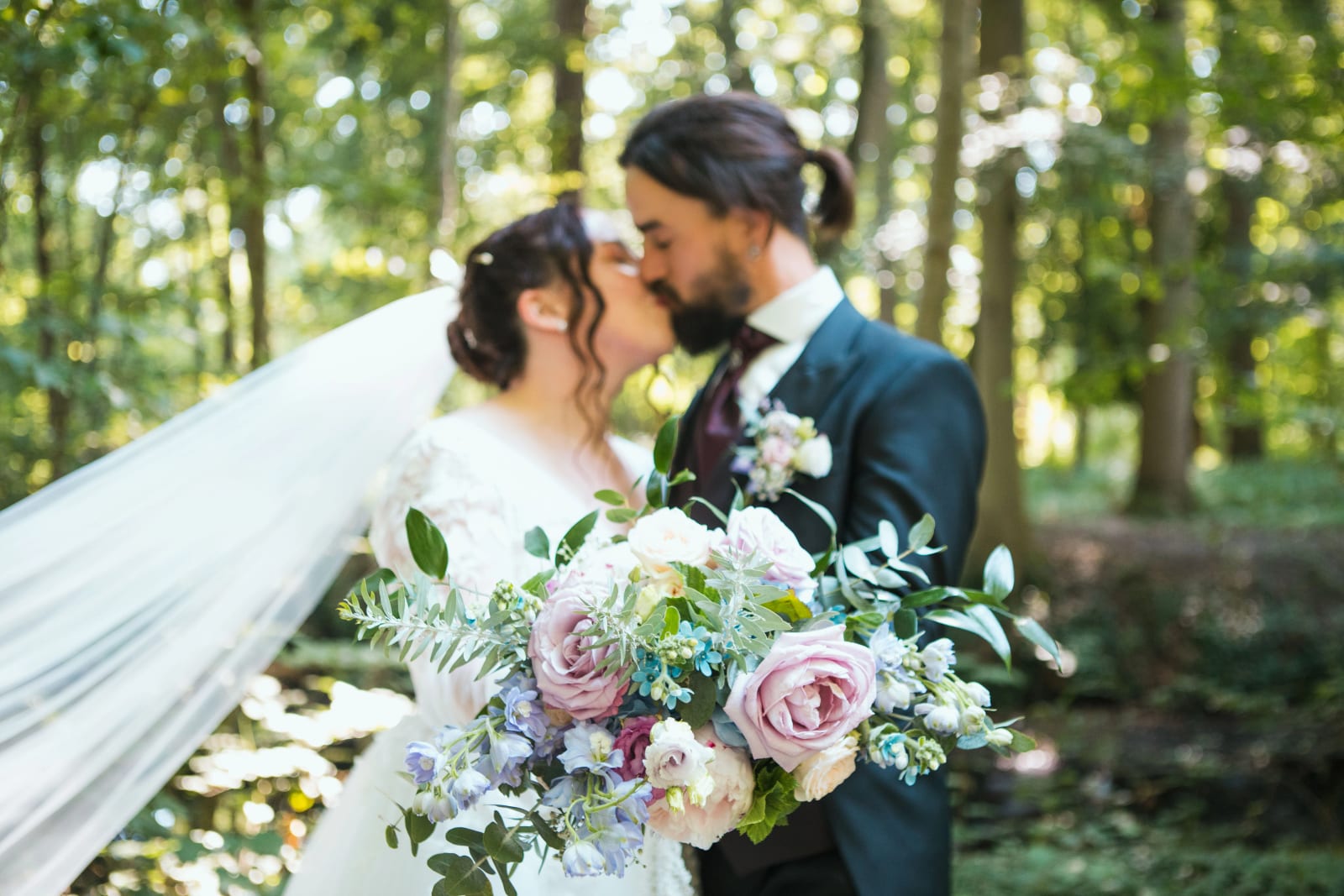 Baiser au voile dans le parc, bouquet de roses pastel au premier plan, mariage au Domaine de l'Orangerie de Villette, par Jean-Baptiste Argyre (Jaysphotography)