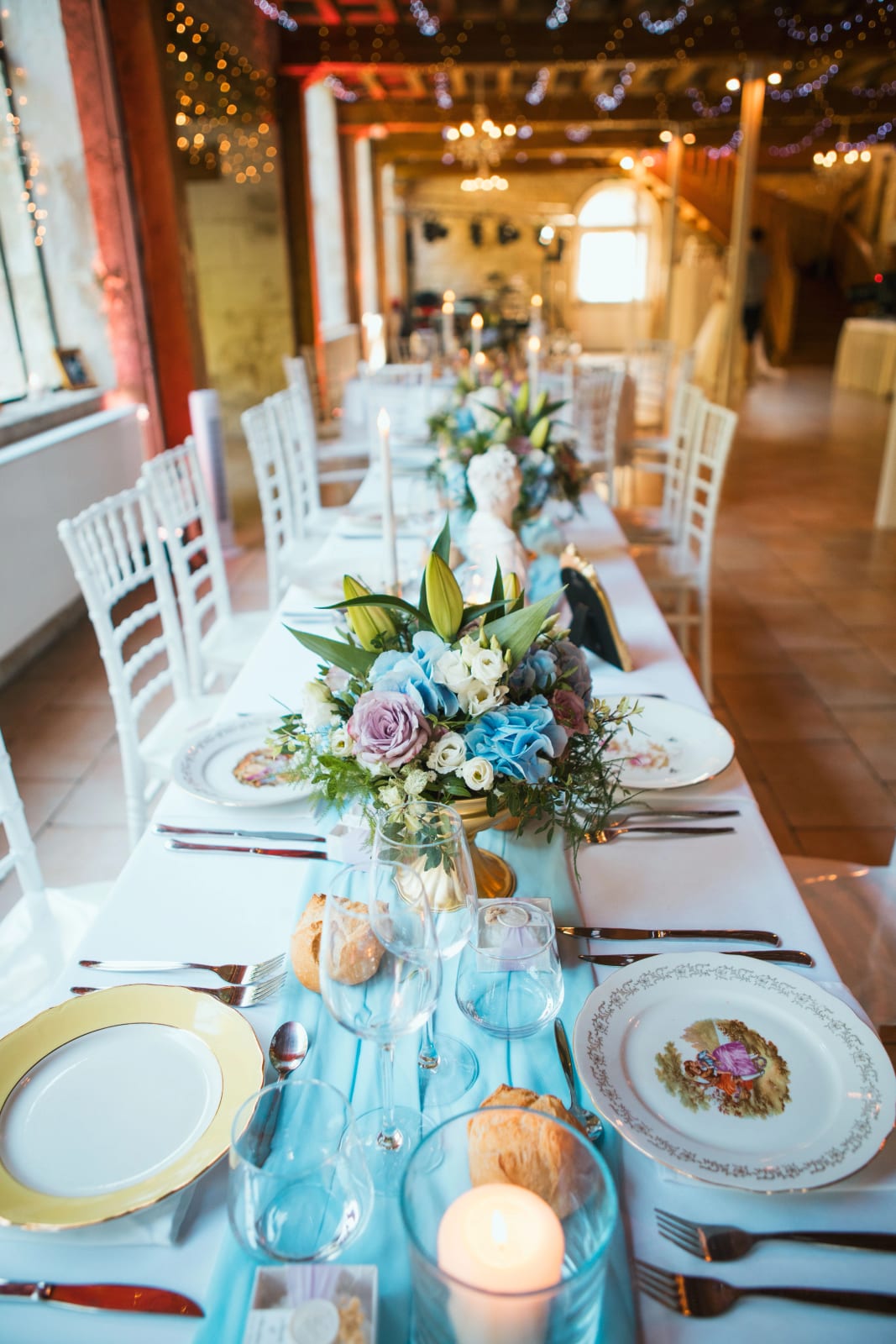 La grande tablée bleu ciel sous les guirlandes de la grange de l'Orangerie, mariage au Domaine de l'Orangerie de Villette, par Jean-Baptiste Argyre (Jaysphotography)