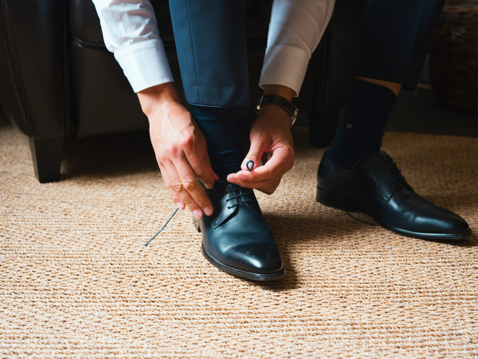 Le marié en chemise blanche noue les lacets de ses derbies noires, assis sur un fauteuil de cuir, mariage au Domaine le Pommerieux, Buzancy, par Jean-Baptiste Argyre (Jaysphotography)
