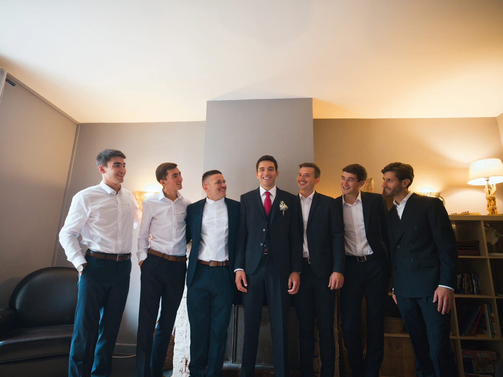 Le marié en costume trois-pièces bleu nuit et cravate rouge entouré de ses amis en chemise blanche dans la chambre, mariage au Domaine le Pommerieux, Buzancy, par Jean-Baptiste Argyre (Jaysphotography)