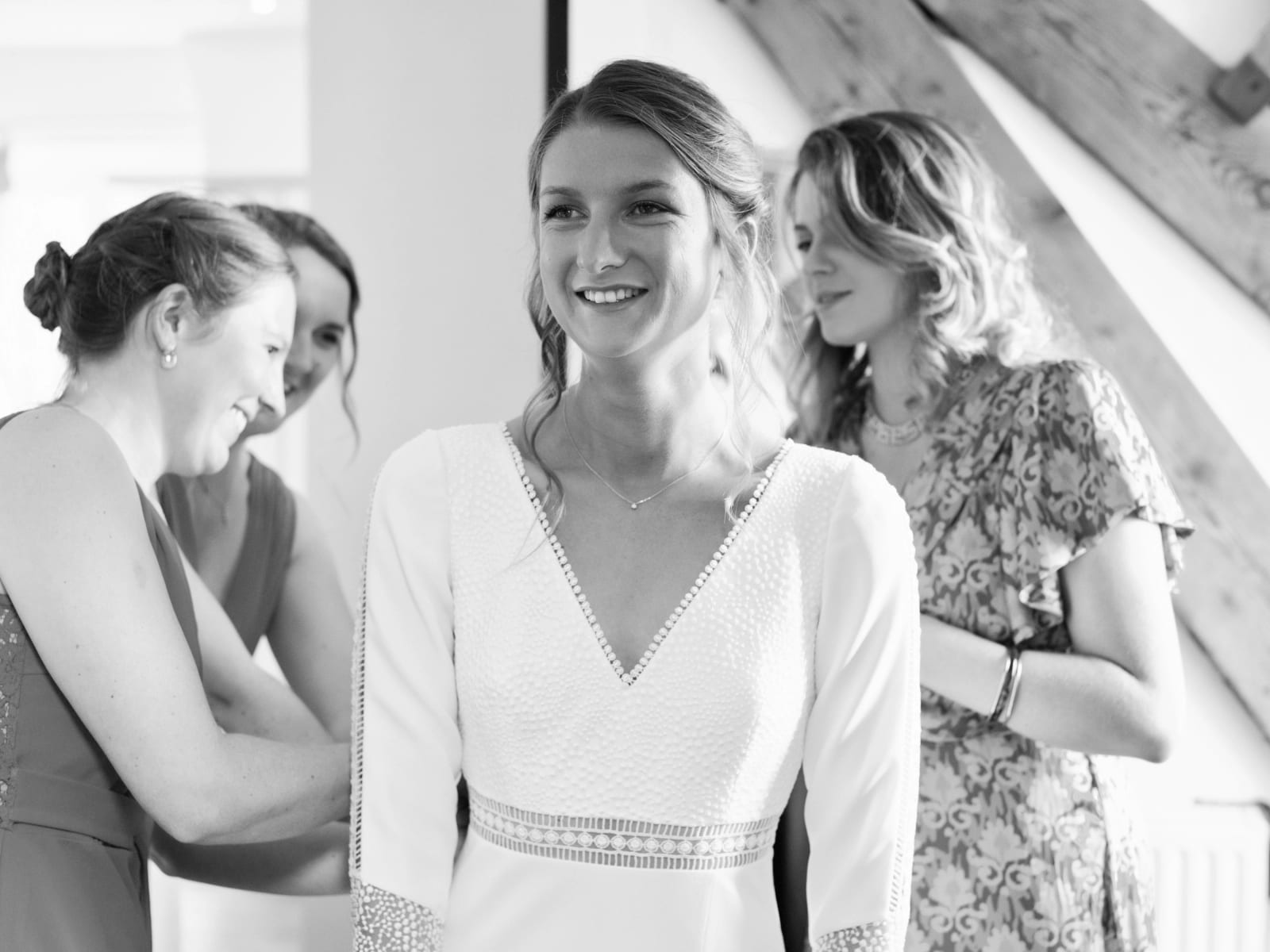 Noir et blanc : les amies de la mariée l'aident à fermer sa robe à col en V, mariage au Domaine le Pommerieux, Buzancy, par Jean-Baptiste Argyre (Jaysphotography)