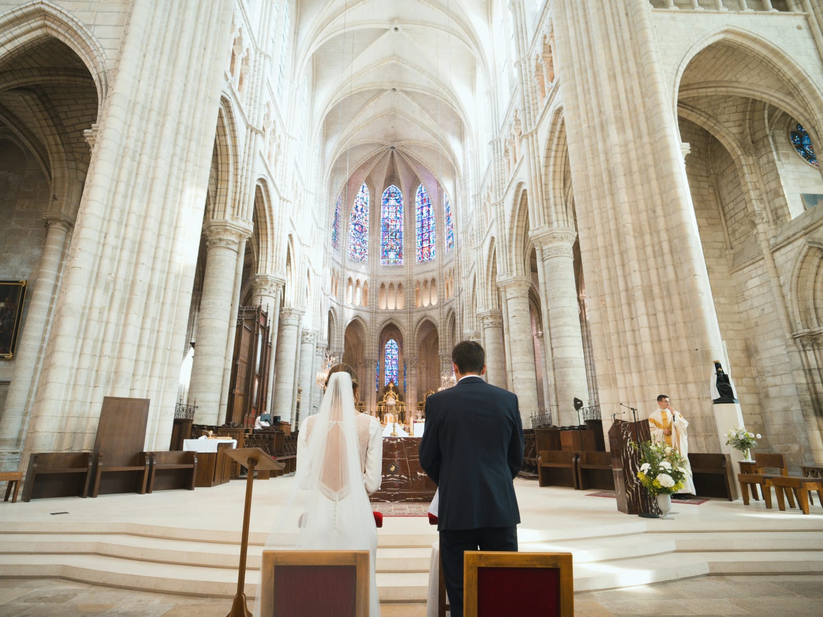 Les mariés de dos devant l'autel de la cathédrale de Soissons, nef gothique et vitraux bleus du chœur, mariage au Domaine le Pommerieux, Buzancy, par Jean-Baptiste Argyre (Jaysphotography)