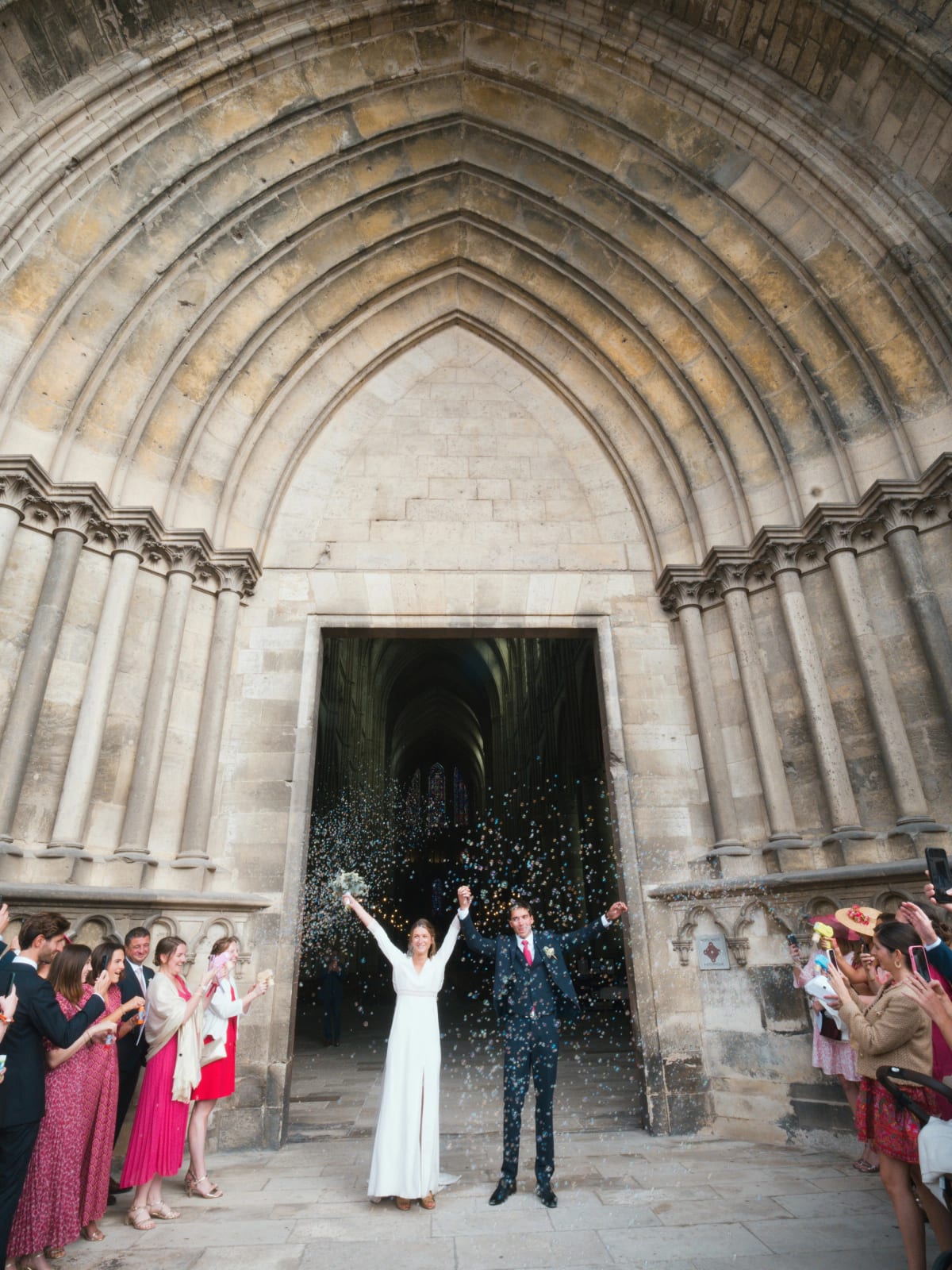 Sortie de la cathédrale de Soissons sous le portail gothique, les mariés lèvent les bras sous les confettis, mariage au Domaine le Pommerieux, Buzancy, par Jean-Baptiste Argyre (Jaysphotography)