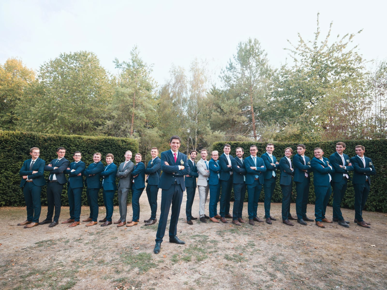 Le marié bras croisés devant une vingtaine d'amis en costume alignés entre deux haies, mariage au Domaine le Pommerieux, Buzancy, par Jean-Baptiste Argyre (Jaysphotography)