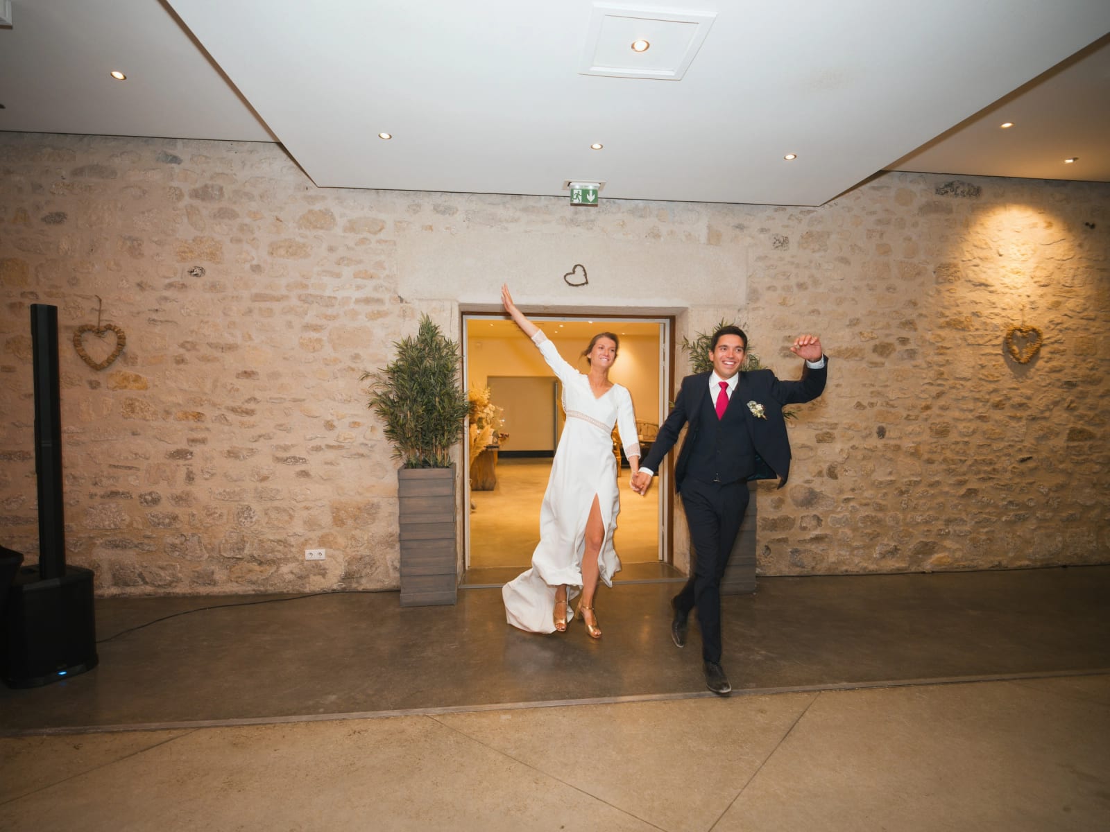 Entrée en salle des mariés main dans la main, la mariée lève le bras, murs de pierre, mariage au Domaine le Pommerieux, Buzancy, par Jean-Baptiste Argyre (Jaysphotography)