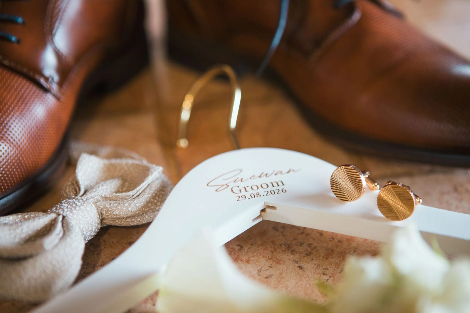 Accessoires du marié : derbies cognac, nœud papillon beige, cintre blanc gravé « Suewan Groom 29.08.2026 » et boutons de manchette dorés, mariage à la Salle Georges Brassens, Villers-Saint-Paul, par Jean-Baptiste Argyre (Jaysphotography)