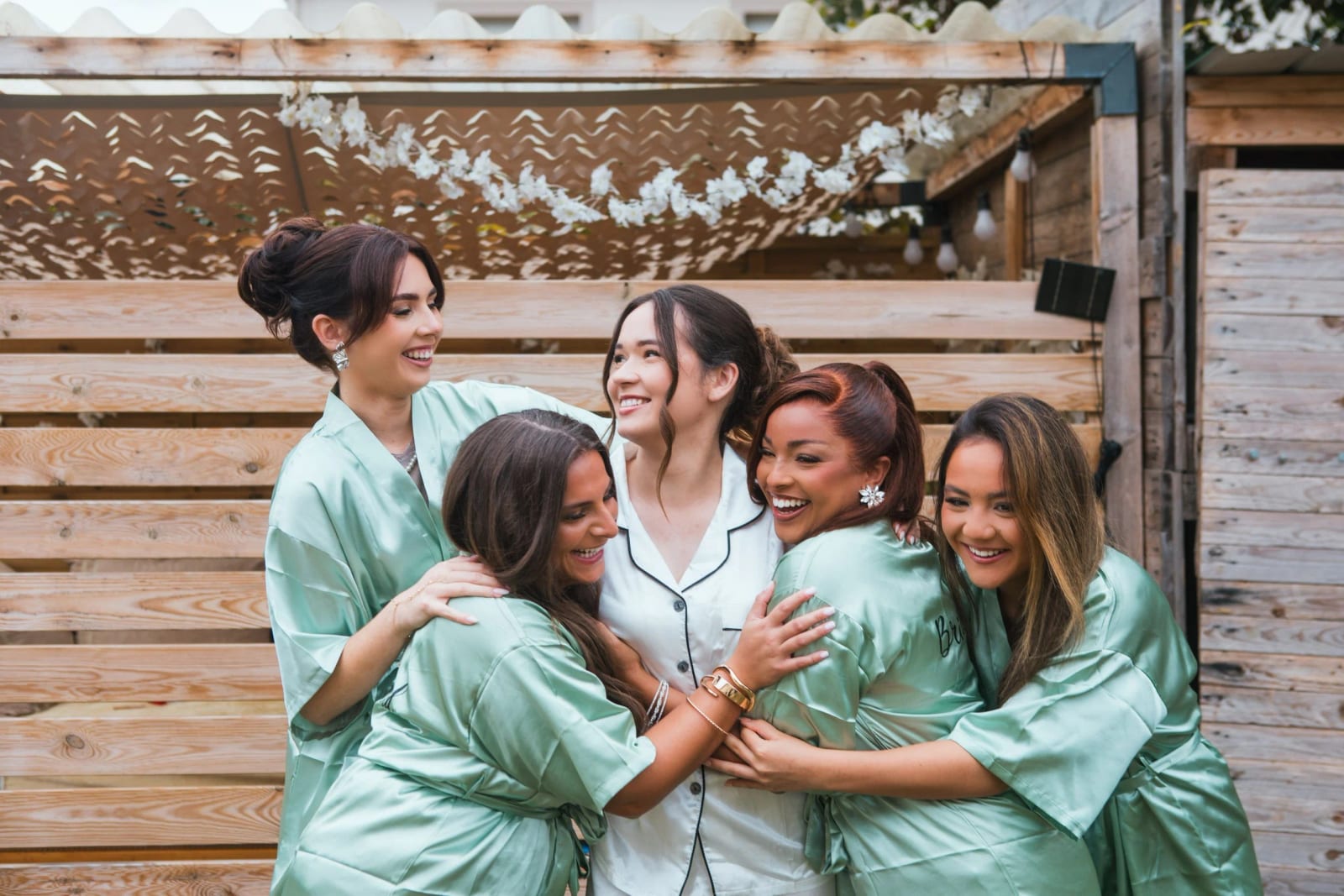 La mariée serrée par ses demoiselles d'honneur en peignoirs de satin vert sauge, éclats de rire, mariage à la Salle Georges Brassens, Villers-Saint-Paul, par Jean-Baptiste Argyre (Jaysphotography)