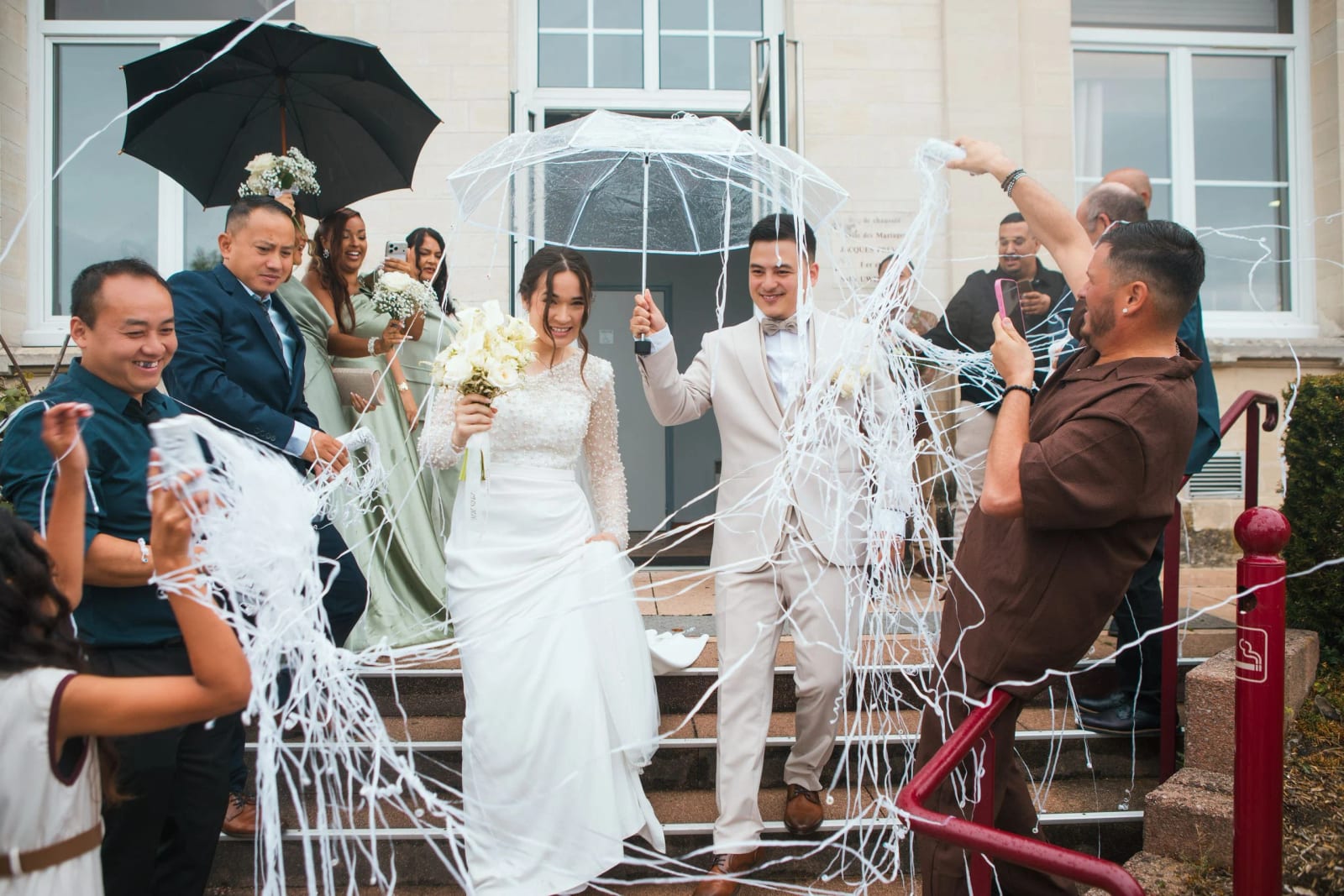 Sortie de la mairie de Villers-Saint-Paul sous les serpentins blancs et deux parapluies, mariage à la Salle Georges Brassens, Villers-Saint-Paul, par Jean-Baptiste Argyre (Jaysphotography)