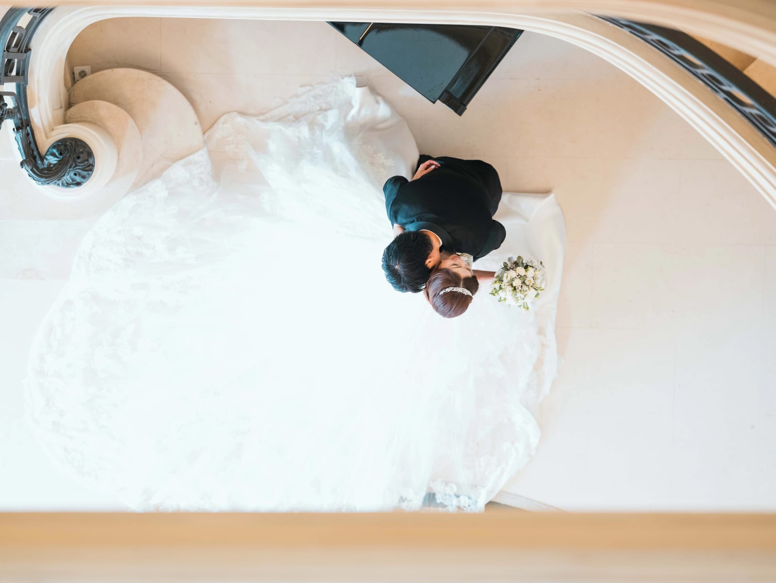 Vue plongeante depuis l'escalier sur les mariés qui s'embrassent, la traîne de dentelle en cercle autour d'eux, mariage au Château Mont Royal, par Jean-Baptiste Argyre (Jaysphotography)