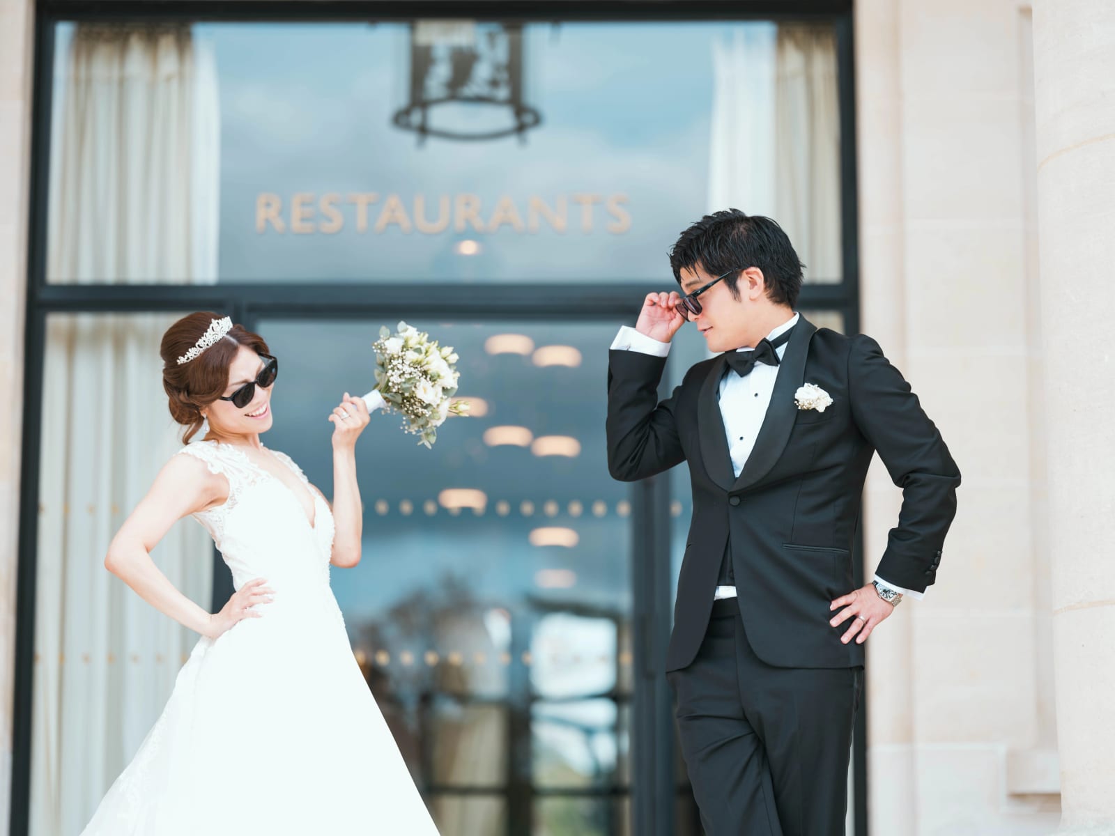 Les mariés en lunettes de soleil prennent la pose devant une porte vitrée marquée Restaurants, mariage au Château Mont Royal, par Jean-Baptiste Argyre (Jaysphotography)