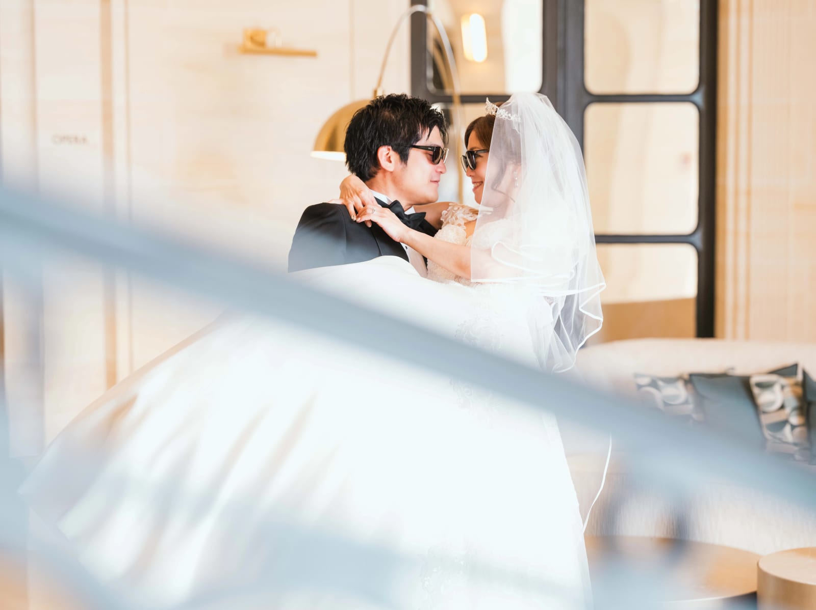 Le marié soulève la mariée en voile, tous deux en lunettes de soleil, à travers une rampe floue, mariage au Château Mont Royal, par Jean-Baptiste Argyre (Jaysphotography)