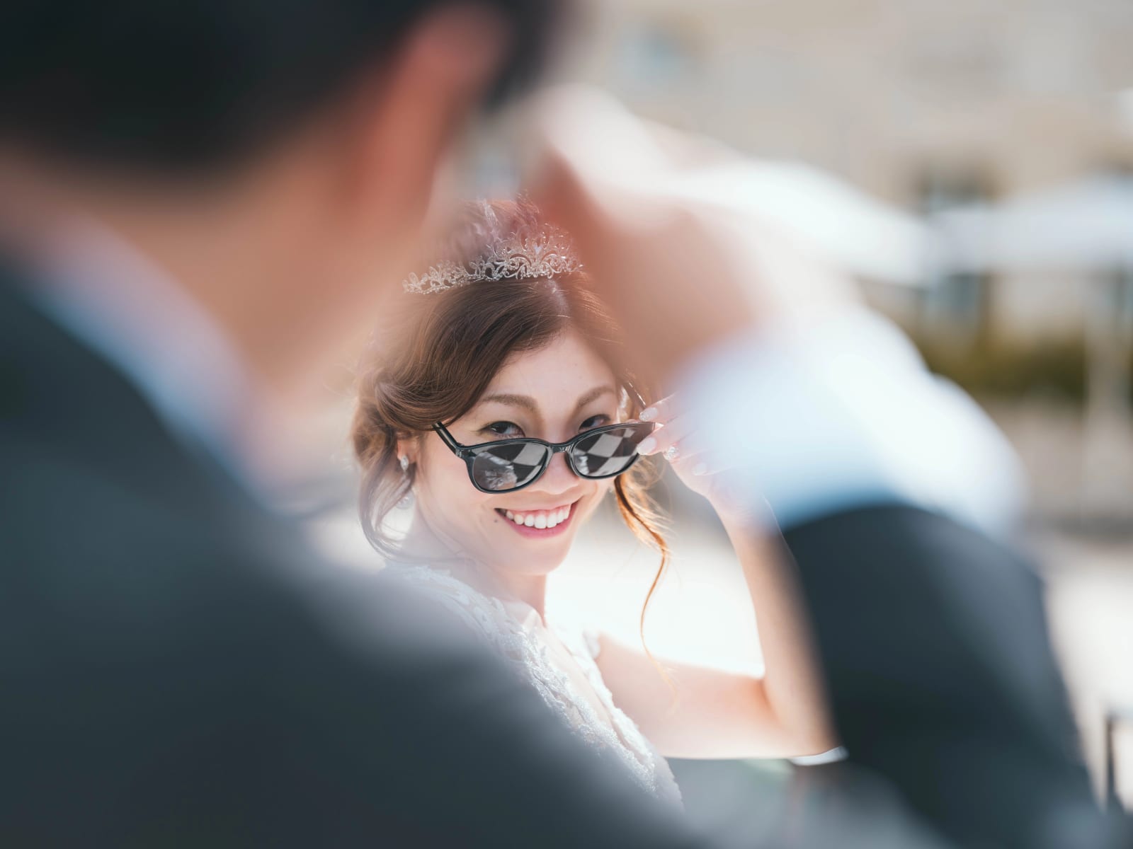 La mariée sourit derrière ses lunettes de soleil, diadème dans les cheveux, épaule du marié floue au premier plan, mariage au Château Mont Royal, par Jean-Baptiste Argyre (Jaysphotography)