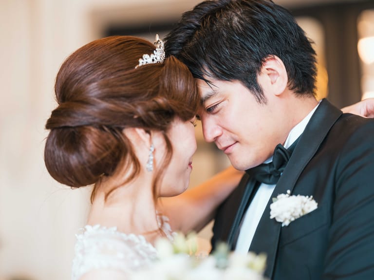 The couple from Japan forehead to forehead in the château hall, the bride's tiara catching the light