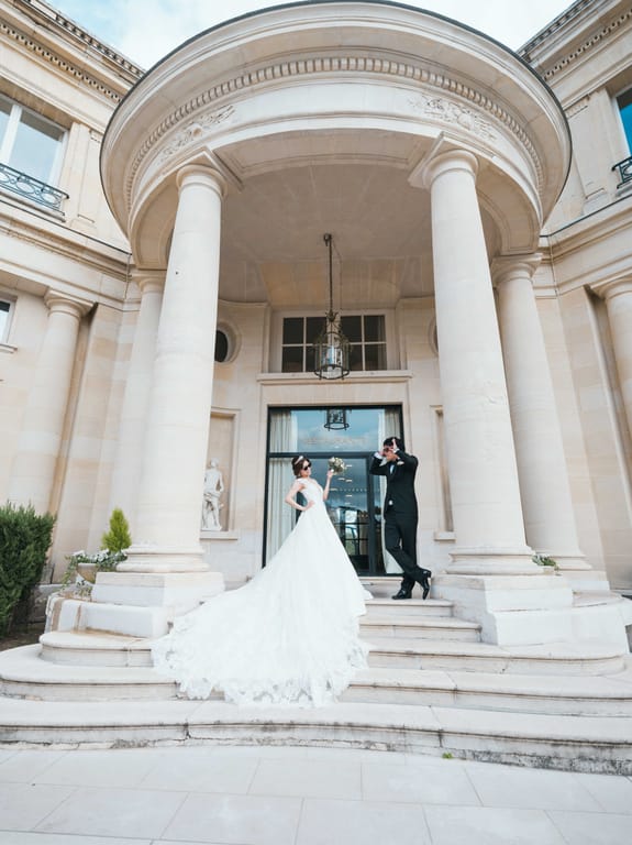 Les mariés sous le portique à colonnes de l'entrée du château, la traîne étalée sur les marches de pierre