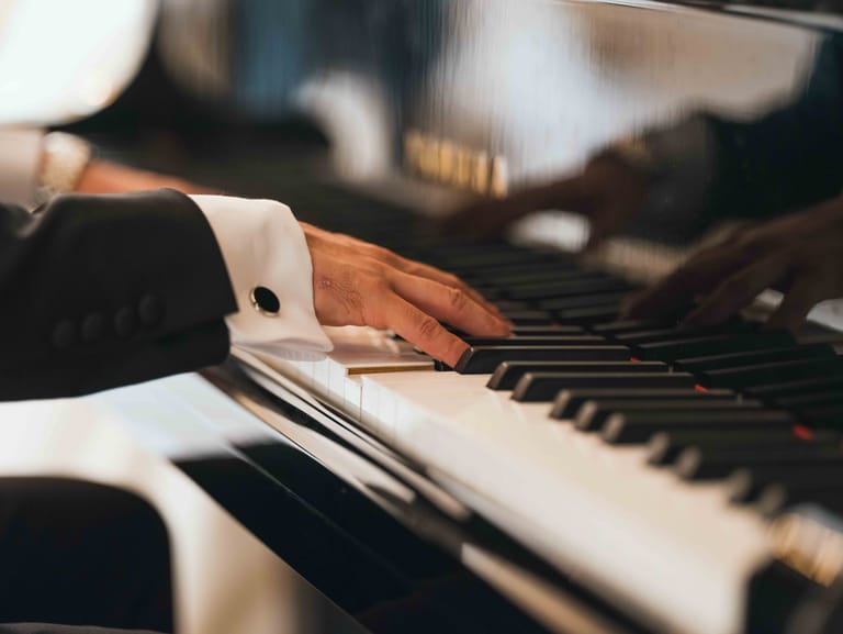 Gros plan sur les mains du marié en smoking au clavier du piano à queue du Château Mont Royal