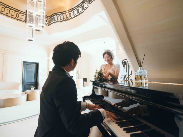 Le marié joue du piano à queue du hall pendant que la mariée l'écoute, accoudée à l'instrument