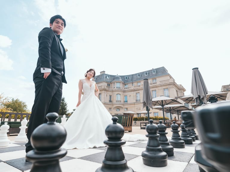 The couple on a giant chessboard on the château rooftop terrace, the façade of the Château Mont Royal behind them